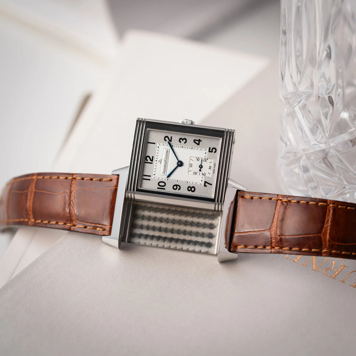 Produktfotografie zeigt die Funktion des Reverso-Mechanismus von der Jaeger-LeCoultre Reverso Grande Taille der Referenz 270.8.62 mit einem teil-guillochiertem, silberfarbenem Zifferblatt an einem braunem Lederband