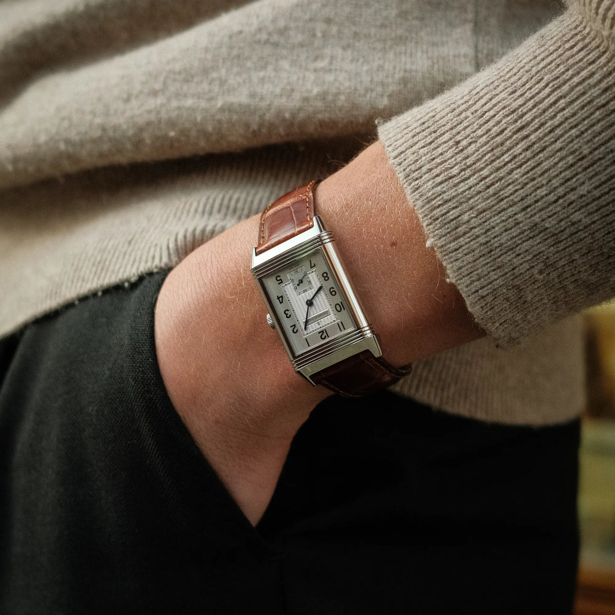 Mann trägt die Jaeger-LeCoultre Reverso Grande Taille der Referenz 270.8.62 mit einem teil-guillochiertem, silberfarbenem Zifferblatt an einem braunem Lederband, während er seine Hand in die Hosentasche steckt