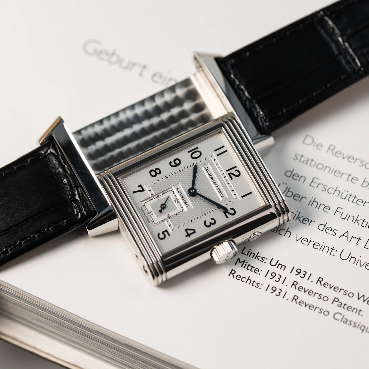 Produktfotografie der Jaeger LeCoultre Reverso Duoface 270.8.54 in Stahl mit Blick auf das weiße Zifferblatt, während der Reverso Mechanismus gezeiugt wird