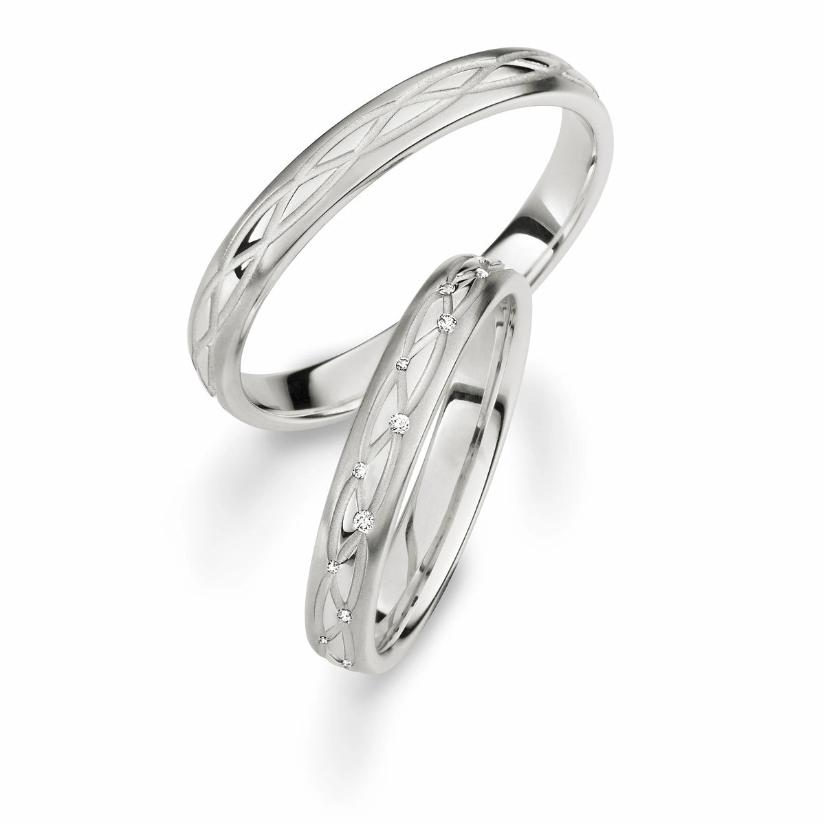 Produktfotografie des weissgoldenen Max Kemper Trauringpaars mit zwei sich umeinander schlingenden eingravierten Linien als Designelement auf der Ringschiene und Diamanten als Verzierung des Damenrings