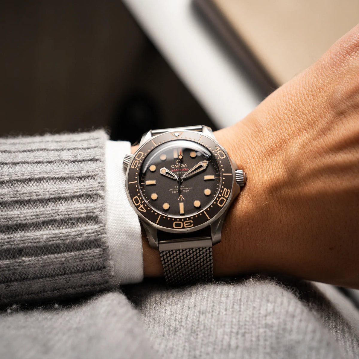 Mann in grauem Pullover trägt die Omega Seamaster 300m Diver No Time To Die Limited Edition aus Titan mit braunem Zifferblatt