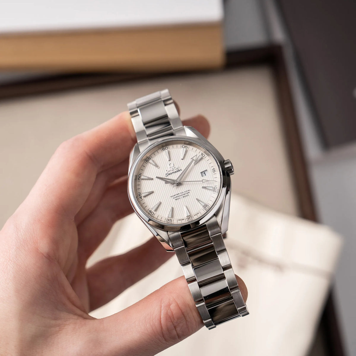 Mann hält die Omega Seamaster Aqua Terra 150M mit 41mm-Gehäuse und einem weißen Zifferblatt mit vertikal verlaufenden Linien in seiner Hand und präsentiert die Uhr in die Kamera