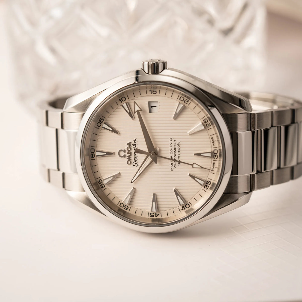 Seitlich auf dem Uhrengehäuse liegenden Omega Seamaster Aqua Terra 150M mit 41mm-Gehäuse und einem weißen Zifferblatt mit vertikal verlaufenden Linien