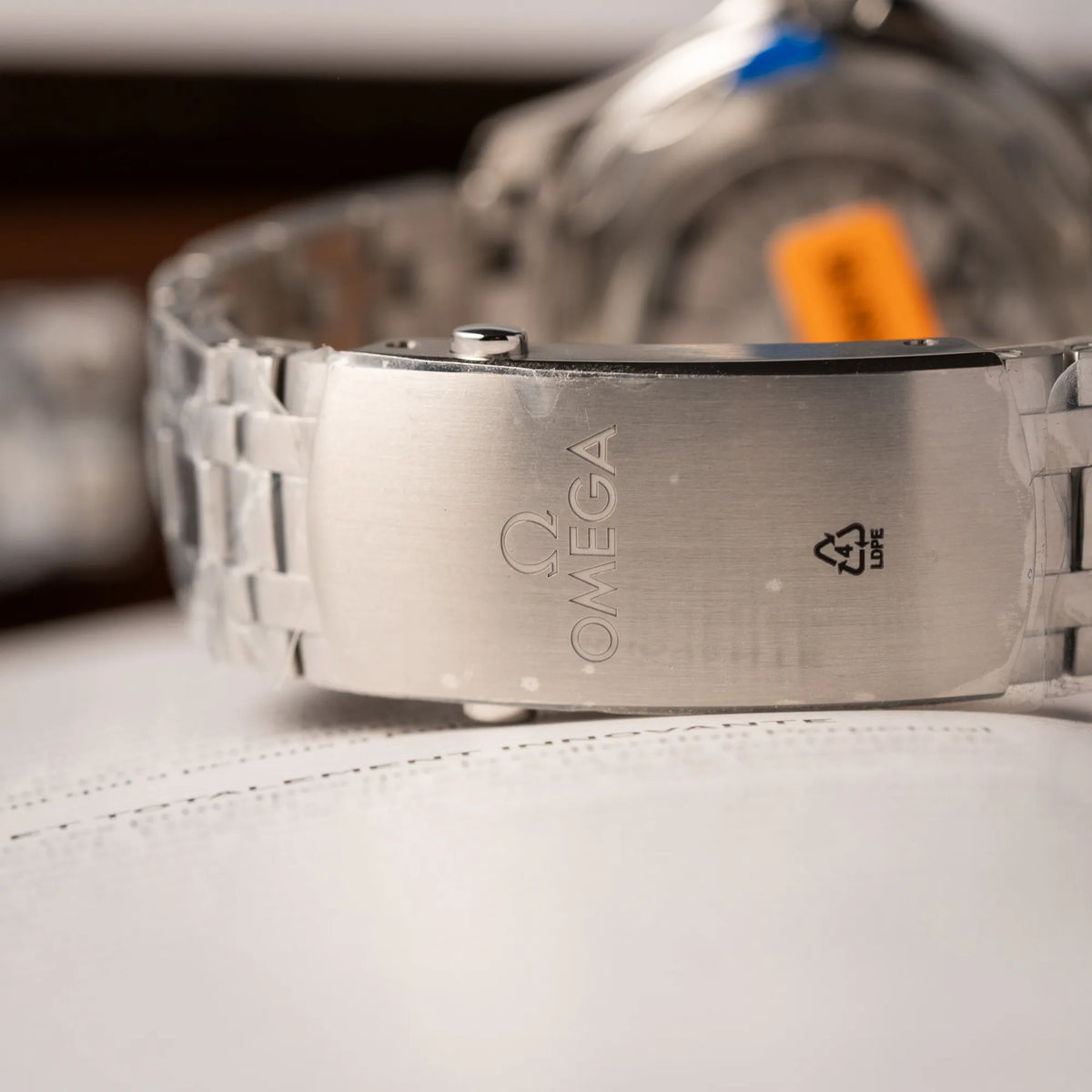 Omega-Faltschliesse der Omega Seamaster Diver 300M der Referenz 210.30.42.20.06.001 mit grauem Zifferblatt im Wellen-Design und blauer Lünette am Edelstahlarmband, welches zum Schutz verklebt wurde