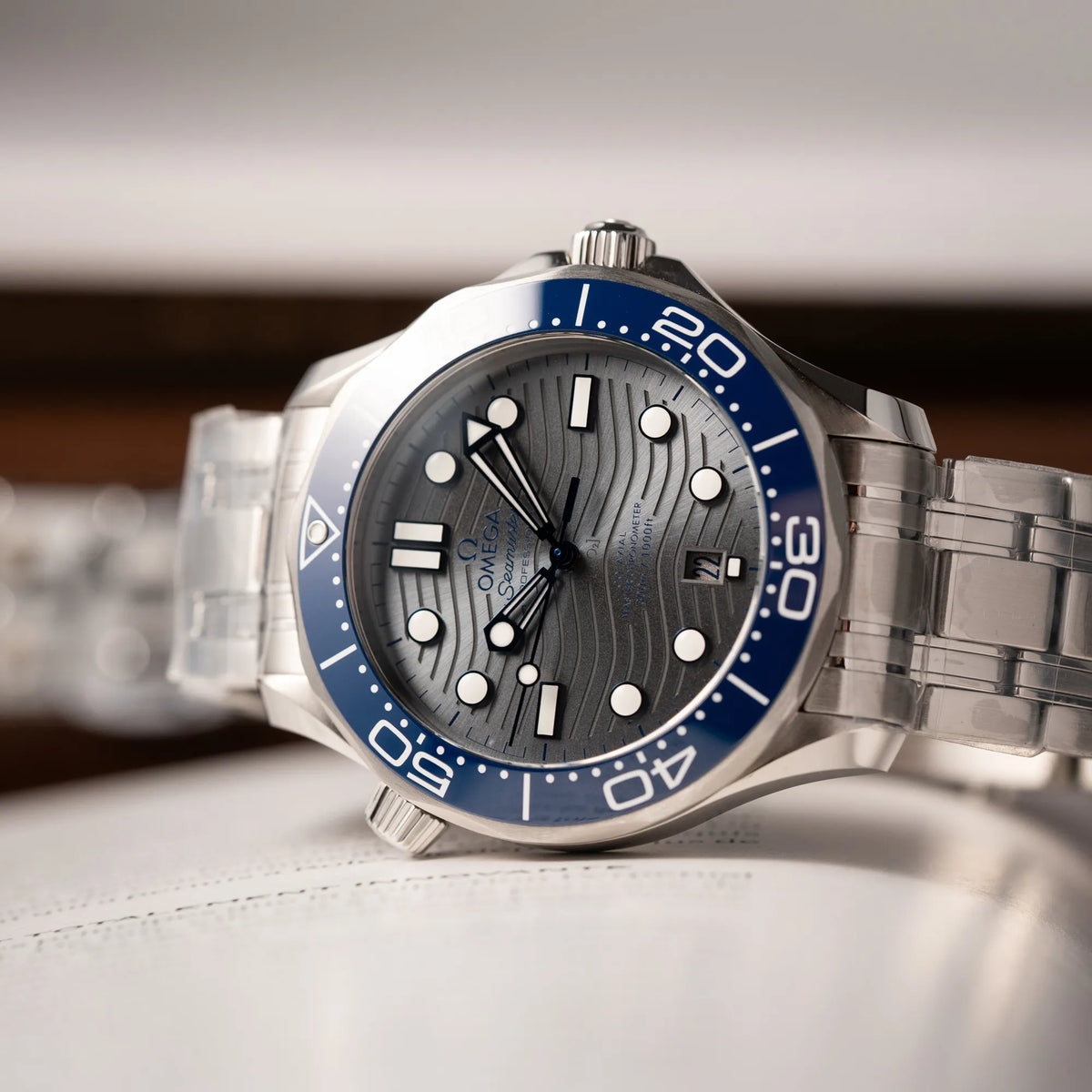 Detailaufnahme der Omega Seamaster Diver 300M der Referenz 210.30.42.20.06.001 mit grauem Zifferblatt im Wellen-Design und blauer Lünette am Edelstahlarmband, welches zum Schutz verklebt wurde