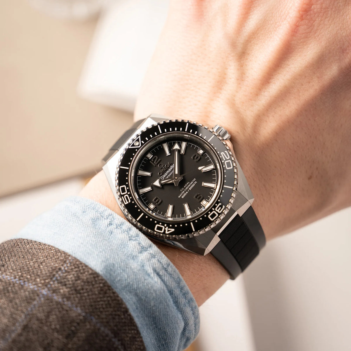 Mann trägt die Omega Seamaster Planet Ocean der Referenz 217.32.42.21.01.001 (4. Generation) mit schwarzem Zifferblatt und Lünette am schwarzen Kautschuk-Armband für einen Wristshot an seinem Handgelenk