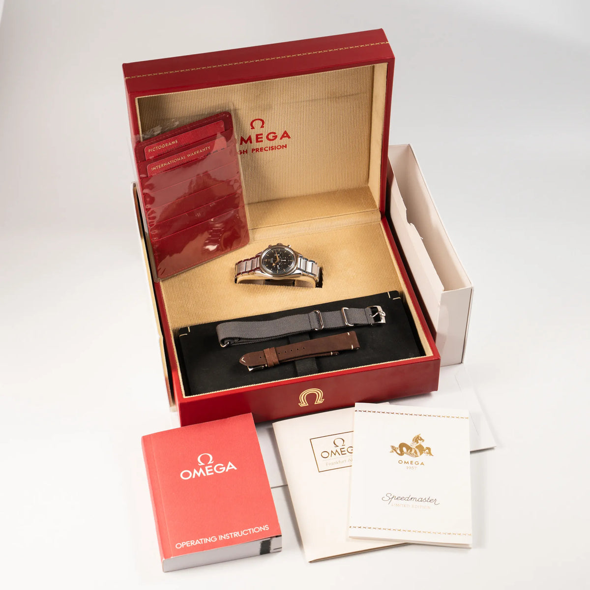 Omega Speedmaster 1957 Trilogy Limited Edition mit einem anthrazitfarbenen Zifferblatt mit Vintage-Look und dem original Omega-Stahlband im Ed-White-Design mit dem Lieferumfang, bestehend aus Box mit Umkarton, Omega Bedienungsanleitung, Garantiekarte, Booklets und zwei zusätzlichen Armbändern in der Leder- und Nato-Ausführung