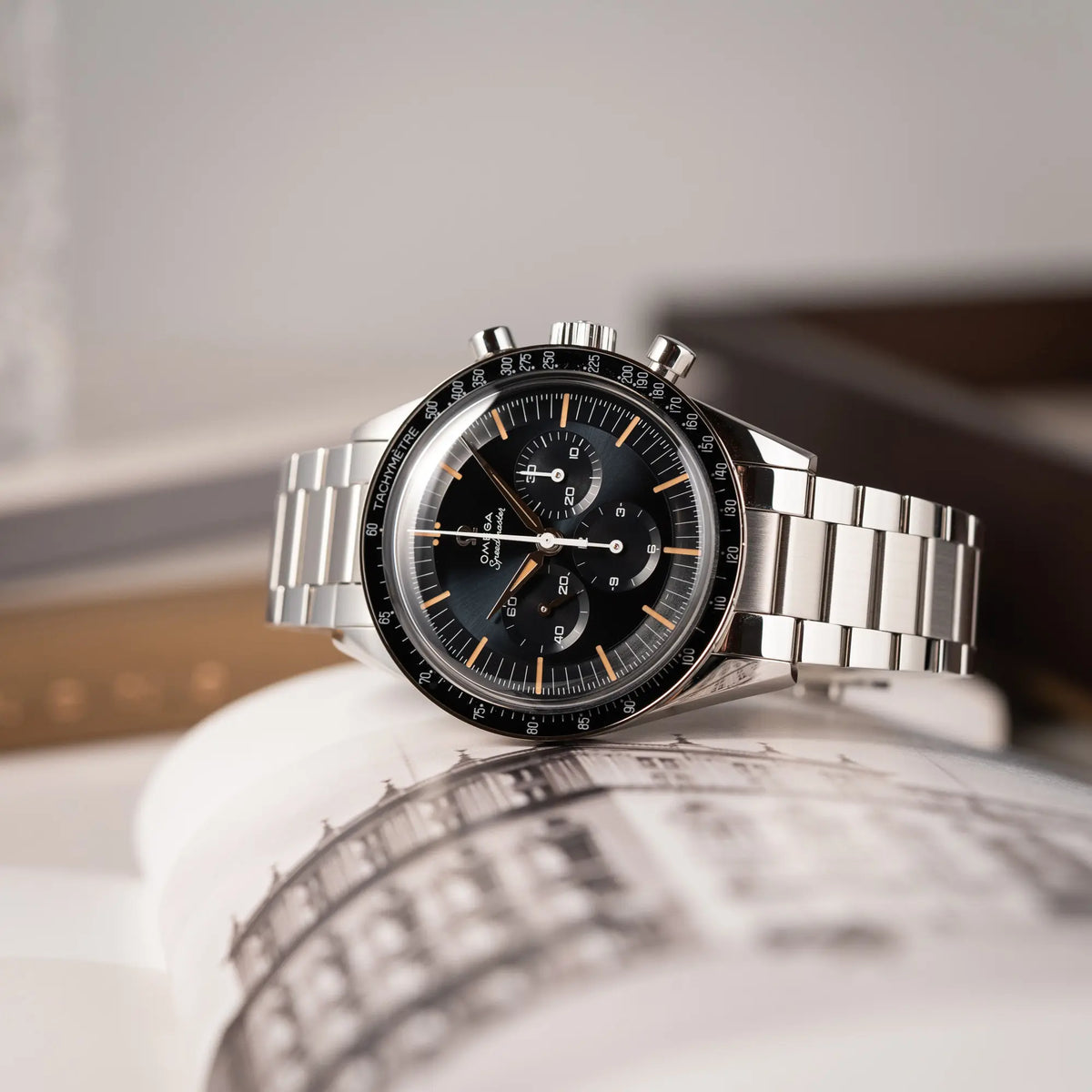 Produktfotografie der seitlich auf dem Uhrengehäuse liegenden Omega Speedmaster FOIS der Referenz 310.30.40.50.06.001 mit dem dunkelblauen Zifferblatt mit dunkel-beigen Indizes im Vintage-Look und einem vom Standard-Modell abgeänderten Stahl-Armband, was beides an das klassische Speedy-Modell erinnert