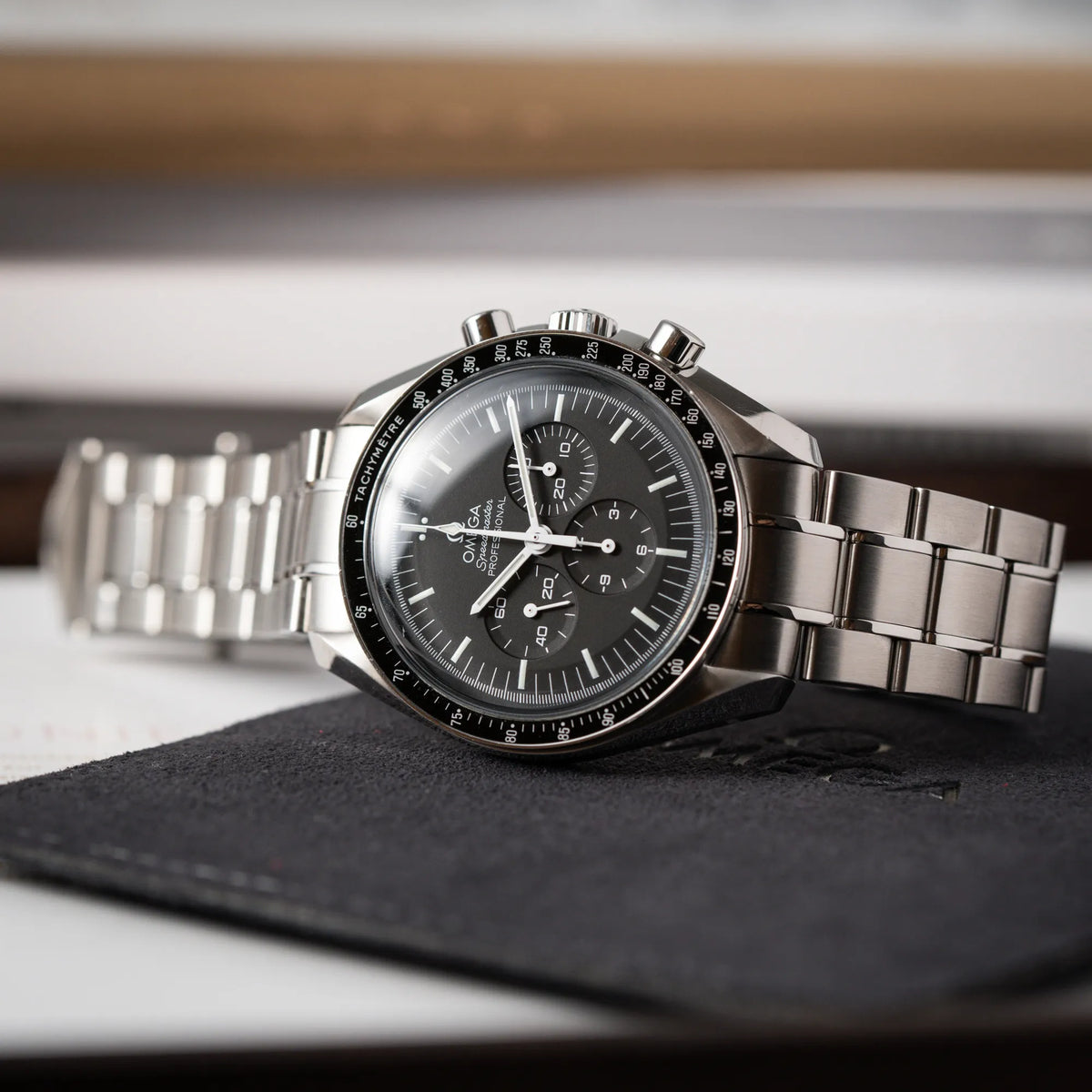 Produktfotografie der seitlich auf dem Uhrengehäuse liegenden Omega Speedmaster Professional Moonwatch der Referenz 311.30.42.30.01.005 in einem 42mm-Gehäuse mit klassischem schwarzen Zifferblatt und verbautem Hesalitglas