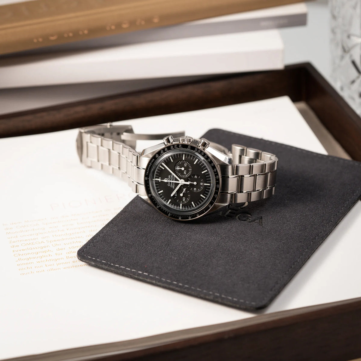 Produktfotografie der Omega Speedmaster Professional Moonwatch der Referenz 311.30.42.30.01.005 in einem 42mm-Gehäuse mit klassischem schwarzen Zifferblatt und verbautem Hesalitglas, während die Uhr auf einem Omega-Lederetui liegt