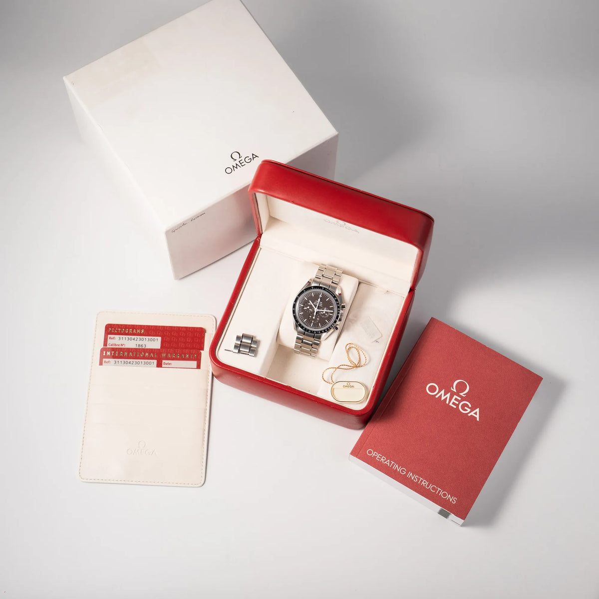 Omega Speedmaster Professional Moonwatch mit einem braunen Zifferblatt zusammen mit dem Lieferumfang, bestehend aus Box mit Umkarton, Hangtag, sowie Garantiekarte