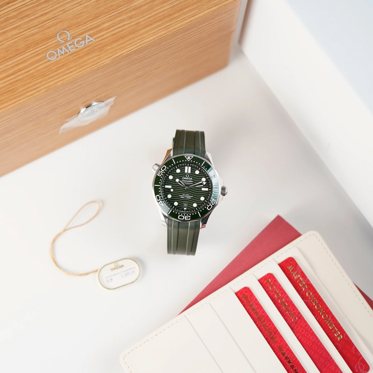 Produktfotografie der oliven Omega Seamaster Professional Diver 300m an einem olivgrünen Kautschukband neben der Box und Garatierkarten