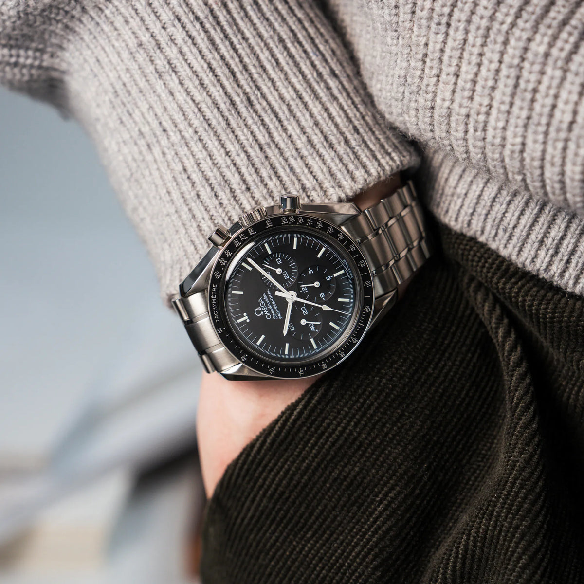 Mann trägt die Omega Speedmaster Moonwatch Professional mit der Referenz 357.50.00 mit dem klassischen schwarzen Zifferblatt an seinem Handgelenk während die Hand in seiner Hosentasche steckt