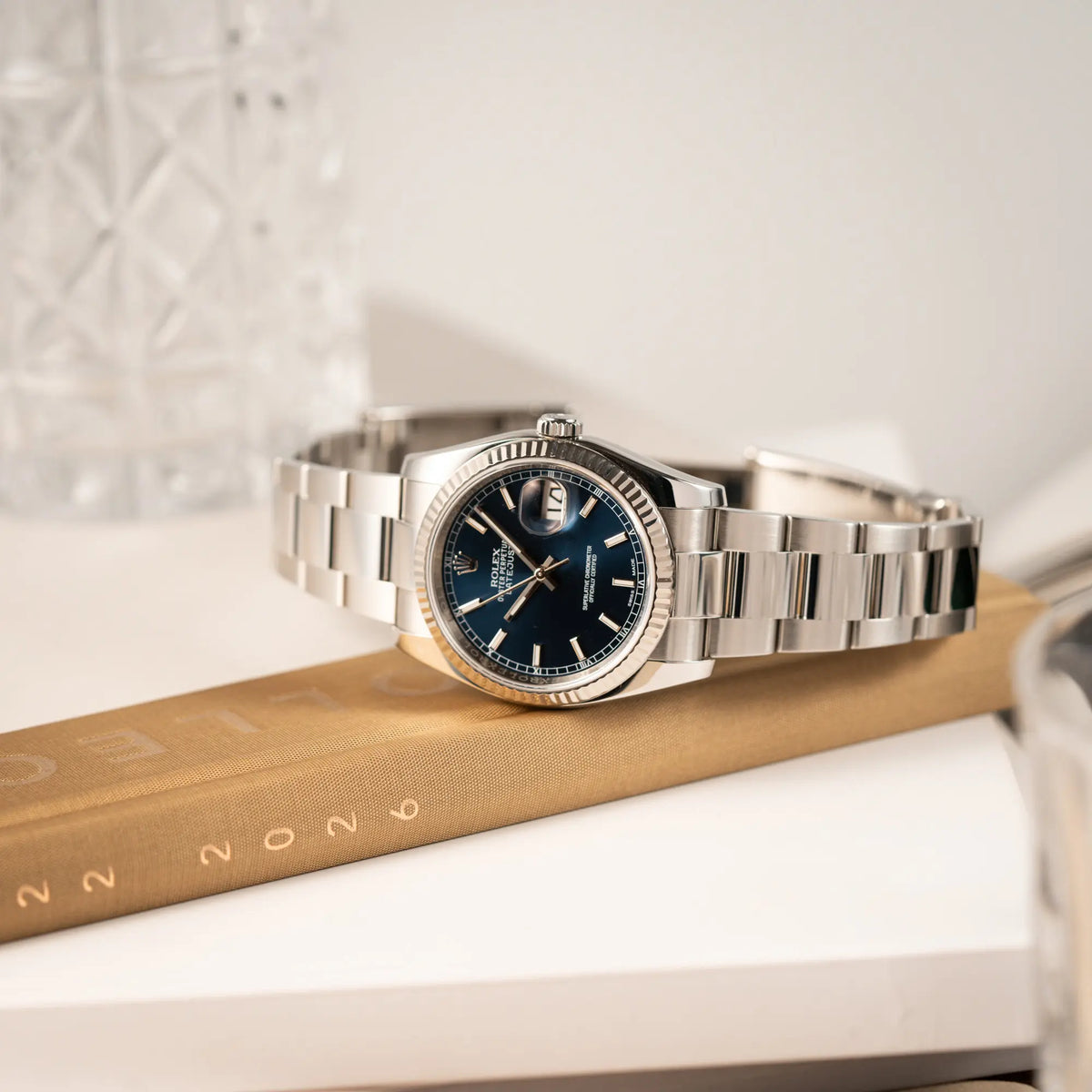 Produktfotografie der seitlich auf der Gehäuseflanke liegenden Rolex Datejust 36 der Referenz 116234 mit geriffelter Lünette und blauem Sonnenschliff-Zifferblatt
