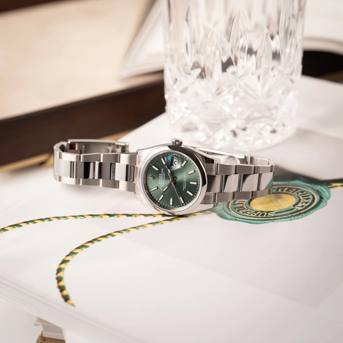 Produktfotografie der seitlich auf dem ehäuse ligenden, mit Stickern teil-verklebte Rolex Datejust 36 der Referenz 126200 mit glatter Lünette am Oyster-Stahlband mit dem Mint-Green-Zifferblatt