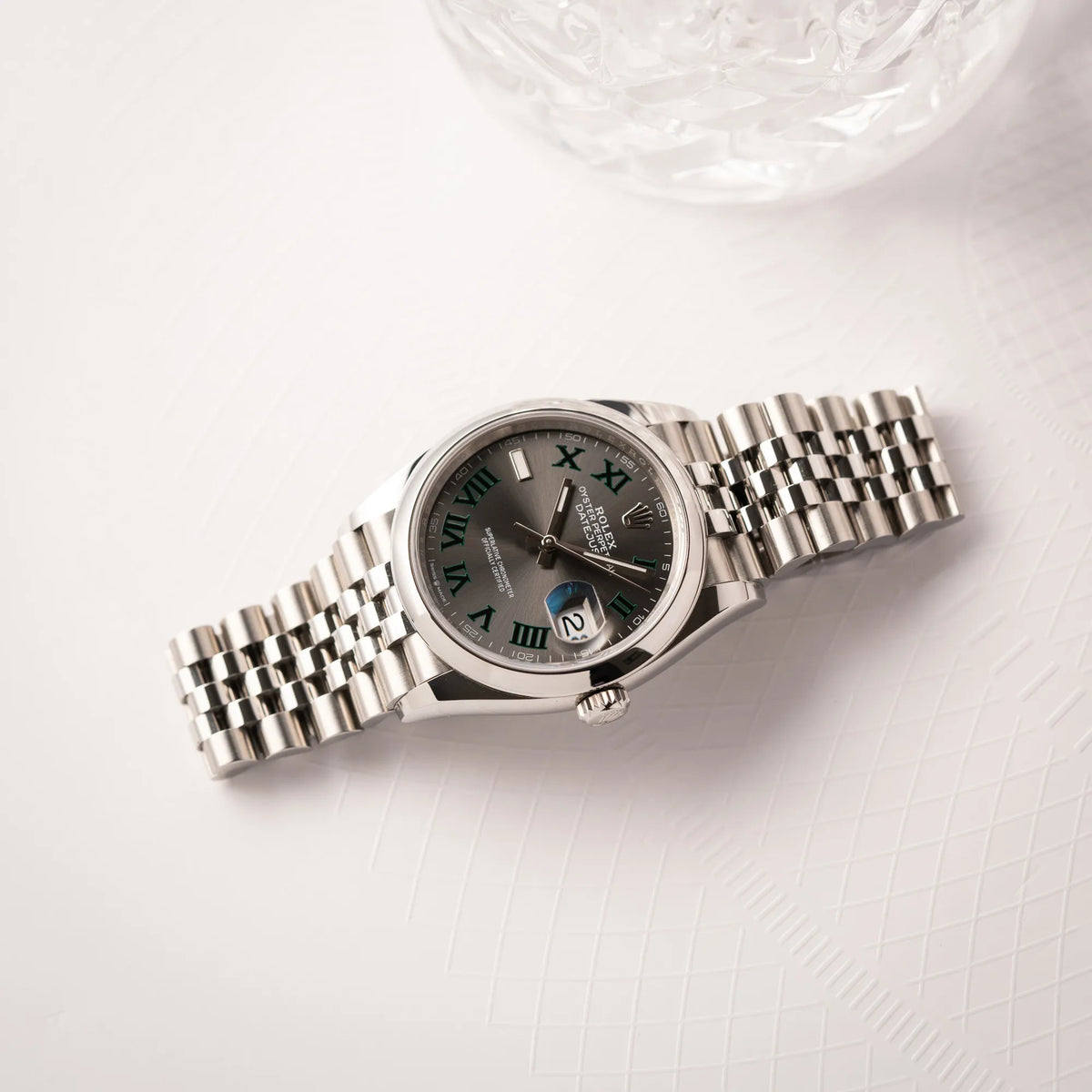 Rolex Datejust 36 Wimbledon der Referenz 126200 mit glatter Lünette, anthrazitfarbenem Zifferblatt und schwarz-grünen, römischen Indizes am Jubillee-Armband liegt flach auf einem Buch