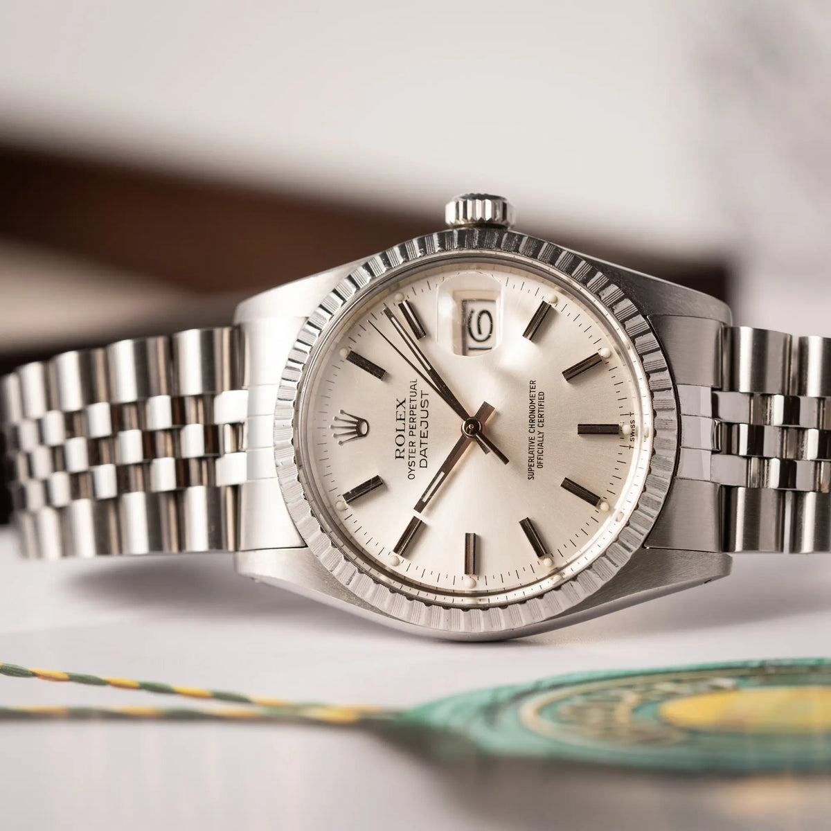 Produktfotografie der seitlich auf dem Uhrengehäuse liegenden Rolex Datejust 36 der Referenz 16030aus Edelstahl mit silberfarbenem Zifferblatt mit Plexiglas am Jubilee-Armband im Vintage-Set