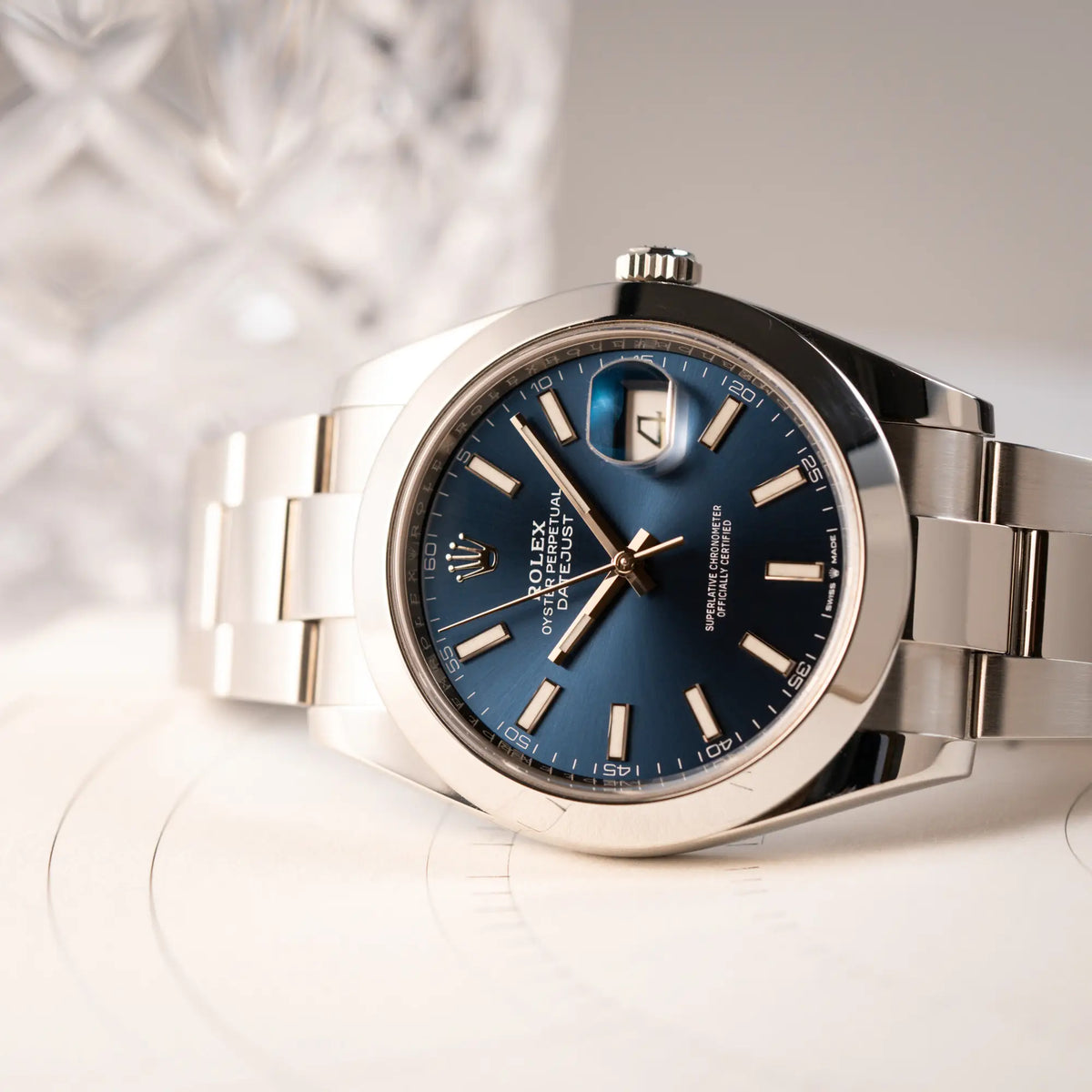 Produktfotografie der seitlich auf dem Gehäuse des Uhrenkopfes liegenden Rolex Datejust 41 der Referenz 126300 mit blauem Zifferblatt, glatter Lünette, am Oyster-Stahlband