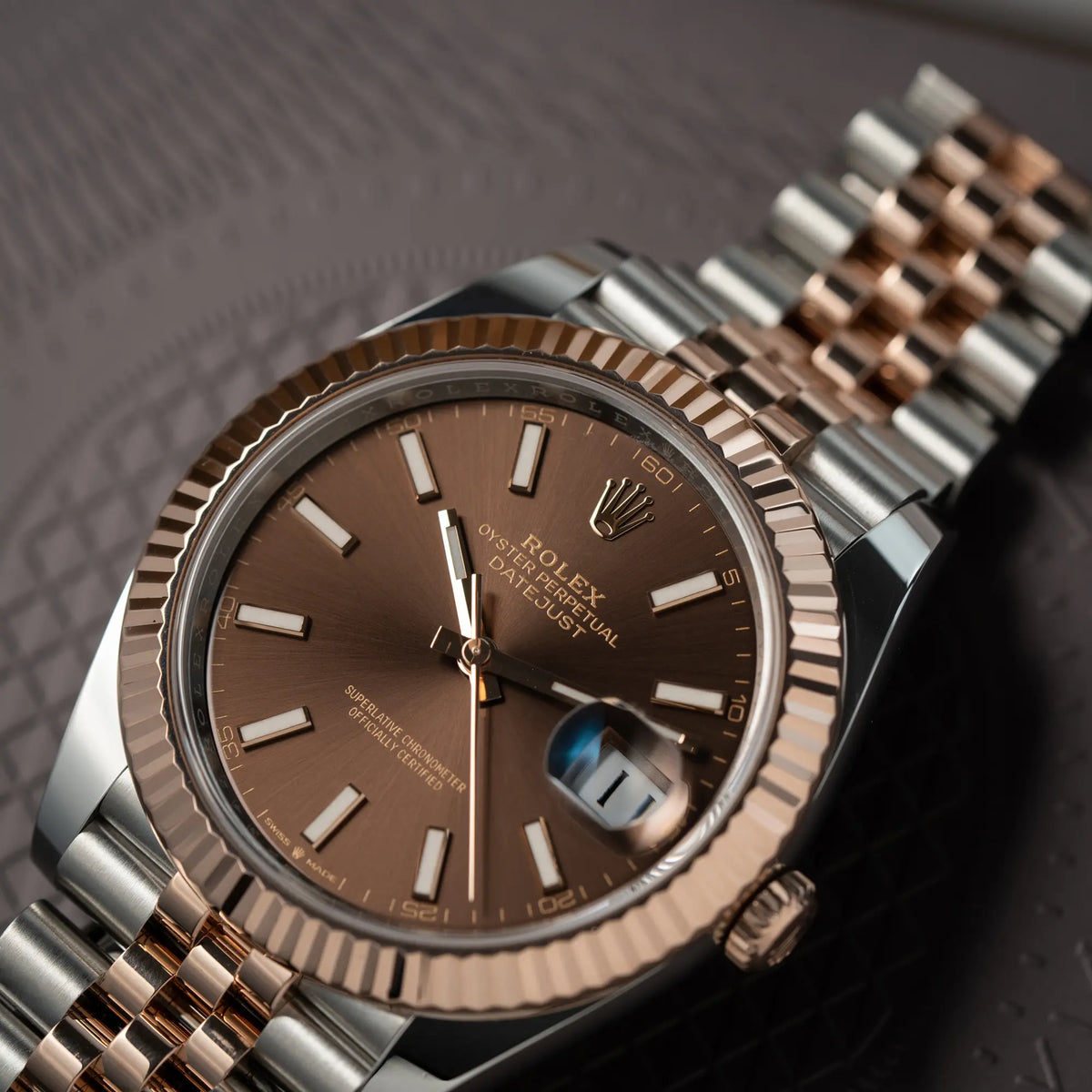 Detailaufnahme der bicolor Rolex Datejust 41 der Referenz 126331 Chocolate in Stahl-Roségold mit einem zum Roségold passenden braunen Zifferblatt am zugehörigen Jubilee-Armband zeigt die roségoldene, geriffelte Lünette und die Sonnenschliff-Struktur des Zifferblatts