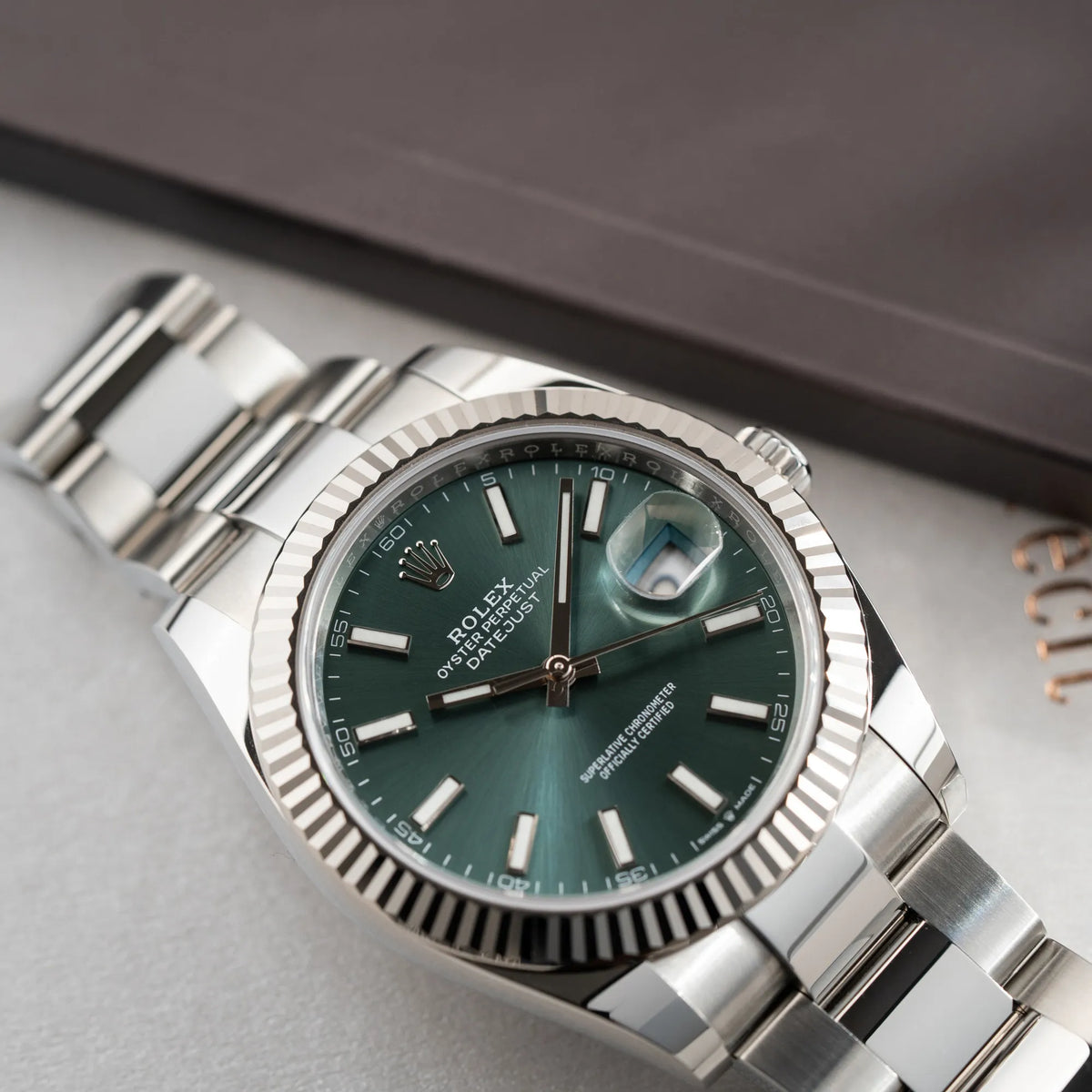 Produktfotografie der Rolex Datejust 41 der Referenz 126334 mit dem grünem Zifferblatt am Oyster-Stahlband mit Fokus auf dem Uhrengehäuse und der geriffelten Lünette