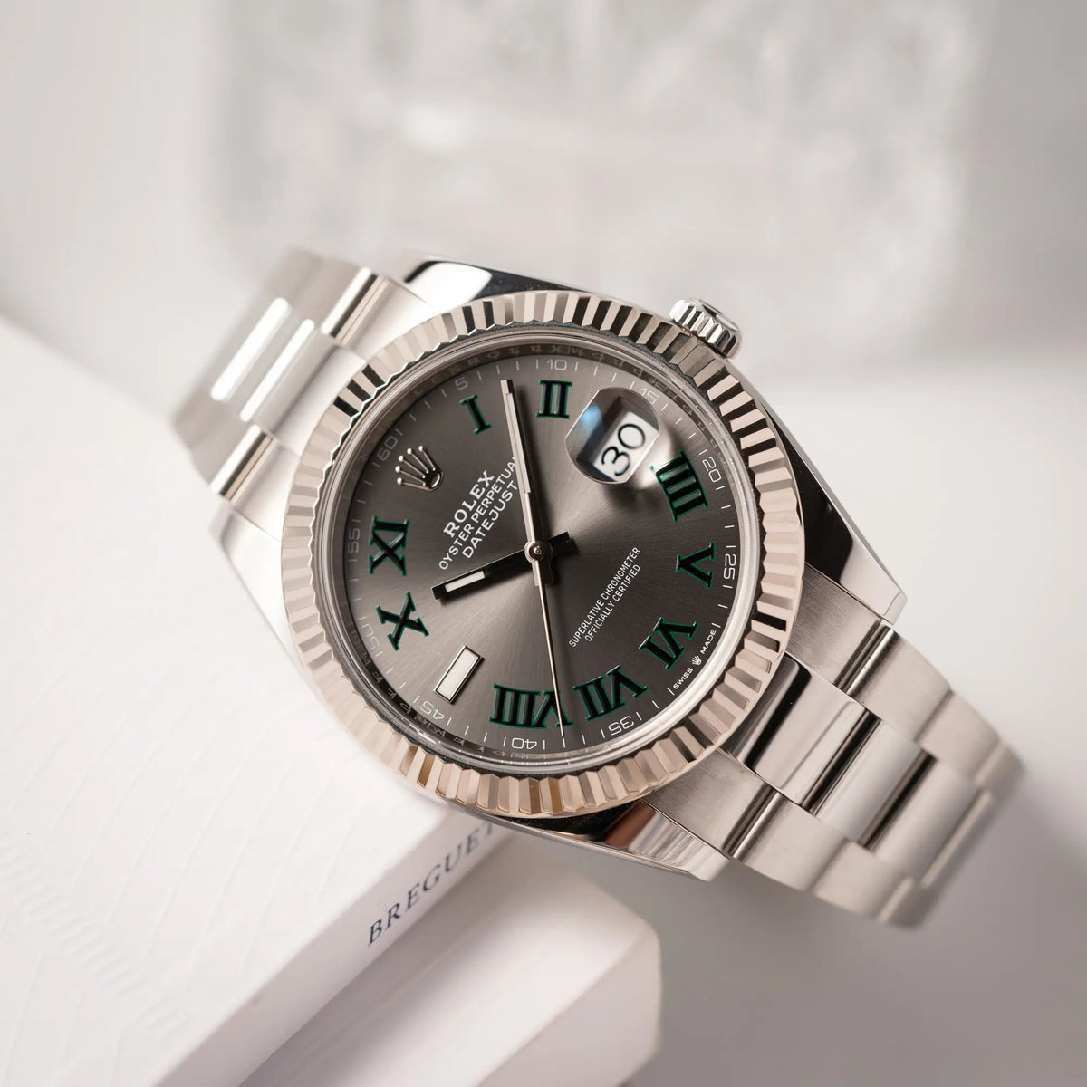 Produktfotografie der Rolex Datejust 41 der Referenz 126334 mit geriffelter Weißgold-Lünette und Oyster-Stahlband mit dem grauen Wimbledon-Zifferblatt mit schwarz-grünen Indizes
