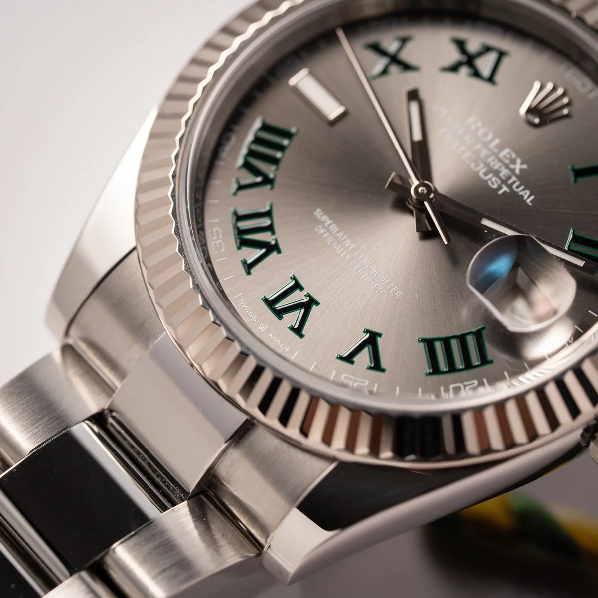 Detailaufnahme zeigt den rechten unteren Bandanstoß der Rolex Datejust 41 der Referenz 126334 mit geriffelter Weißgold-Lünette und Oyster-Stahlband mit dem grauen Wimbledon-Zifferblatt mit schwarz-grünen Indizes
