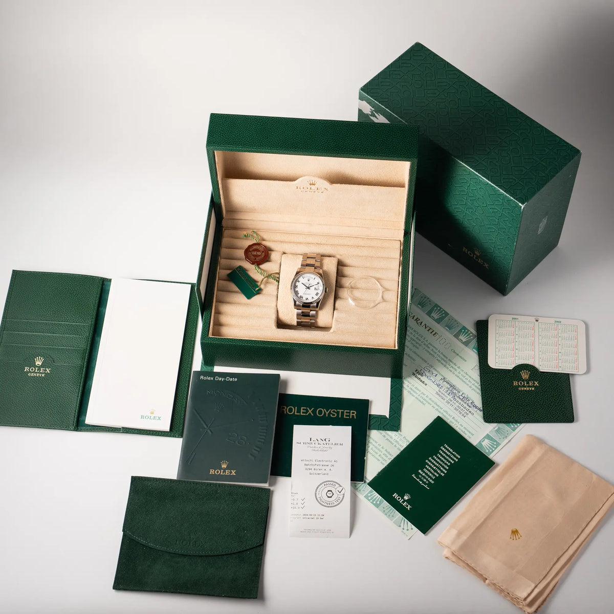 Lieferumfang zu der Rolex Day-Date 36 Armbanduhr in Weißgold der Referenz 118239 mit weißem Zifferblatt mit römischen Indizes am Oyster-Weißgold-Armband, bestehend aus Boc mit Umkarton, allen Booklets, Poliertuch, Lünetten-Schutz, Hangtags, Travel-Etui, Rolex-Kalender 2003, und original Papieren