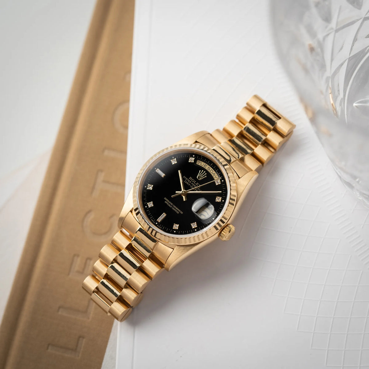 Rolex Day-Date 36 der Referenz 18238 in Gelbgold mit schwarzen Diamond-Dial am President-Armband liegt flach auf dem Uhrenarmband