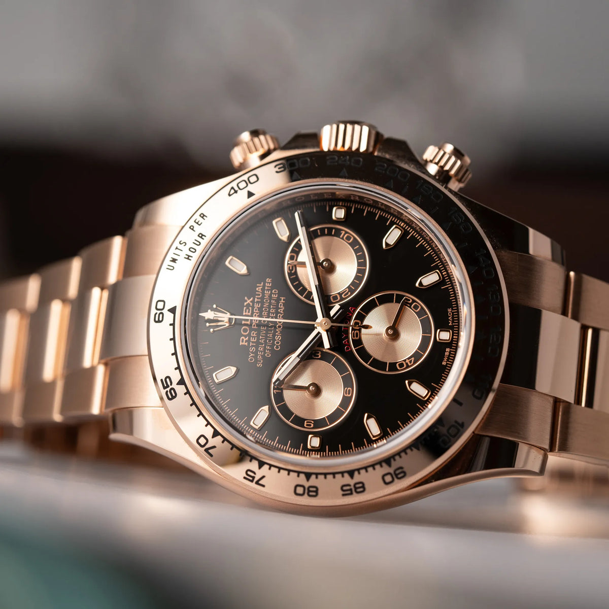 Produktfotografie zeigt die Rolex Daytona Chronograph-Armbanduhr der Referenz 116505 in Everrose-Roségold mit schwarzem Zifferblatt am Oyster-Roségold-Band, während die Uhr seitlich auf dem Gehäuse liegt