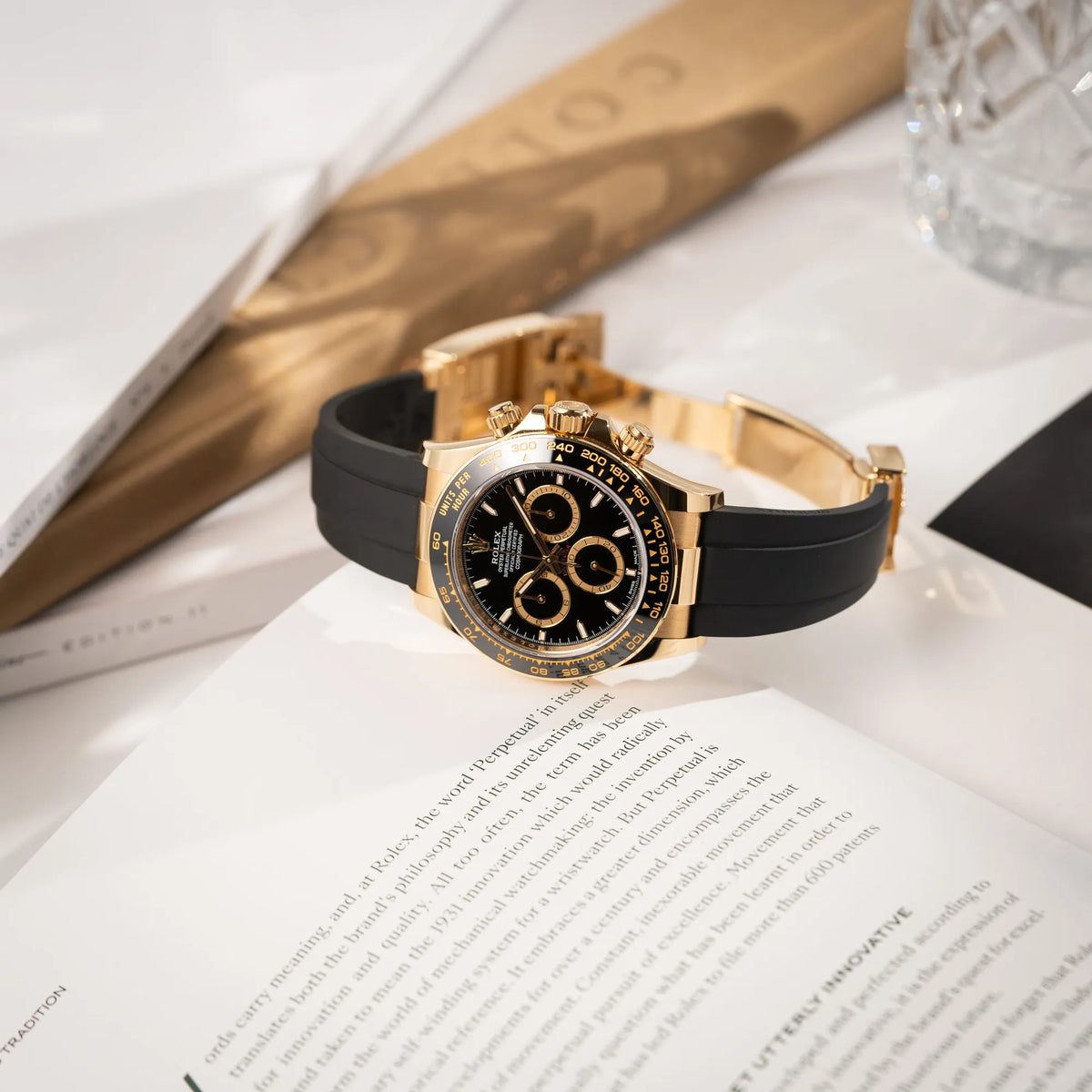 Produktfotografie der seitlich auf dem Gehäuse liegenden Rolex Daytona 126518LN mit Gelbgold-Gehäuse und schwarzem Zifferblatt am schwarzen Oysterflex-Armband aus Kautschuk