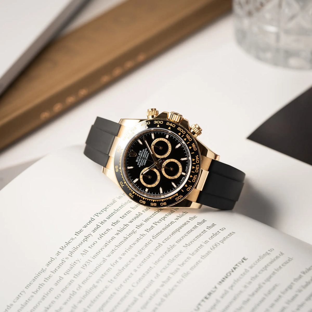 Produktfotografie der Rolex Daytona 126518LN mit Gelbgold-Gehäuse und schwarzem Zifferblatt am schwarzen Oysterflex-Armband aus Kautschuk, während die Uhr auf einem Rolex-Buch liegt