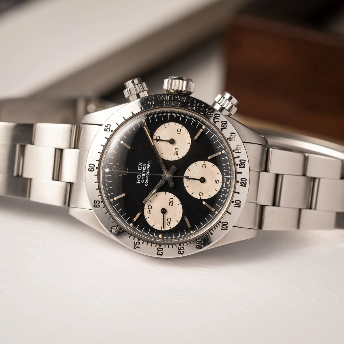 Nahe Produktfotografie der auf dem seitlichen Uhrengehäuse liegenden Rolex Daytona der Referenz 6265 mit Sigma-Dial in schwarz und weißen Sub-Dials im 37mm-Gehäuse aus den 70er Jahren