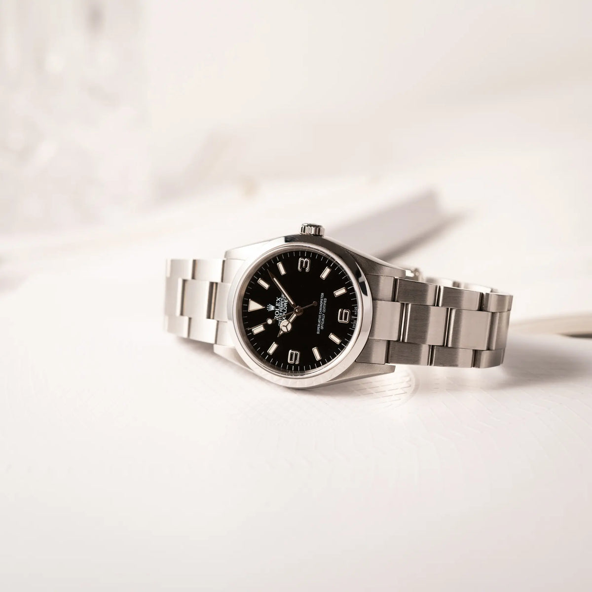 Produktfotografie der seitlich auf dem Uhrengehäuse liegenden Rolex Explorer 36 der Referenz 114270 mit dem klassischen schwarzen 3-6-9-Explorer-Zifferblatt am Oyster-Stahlband
