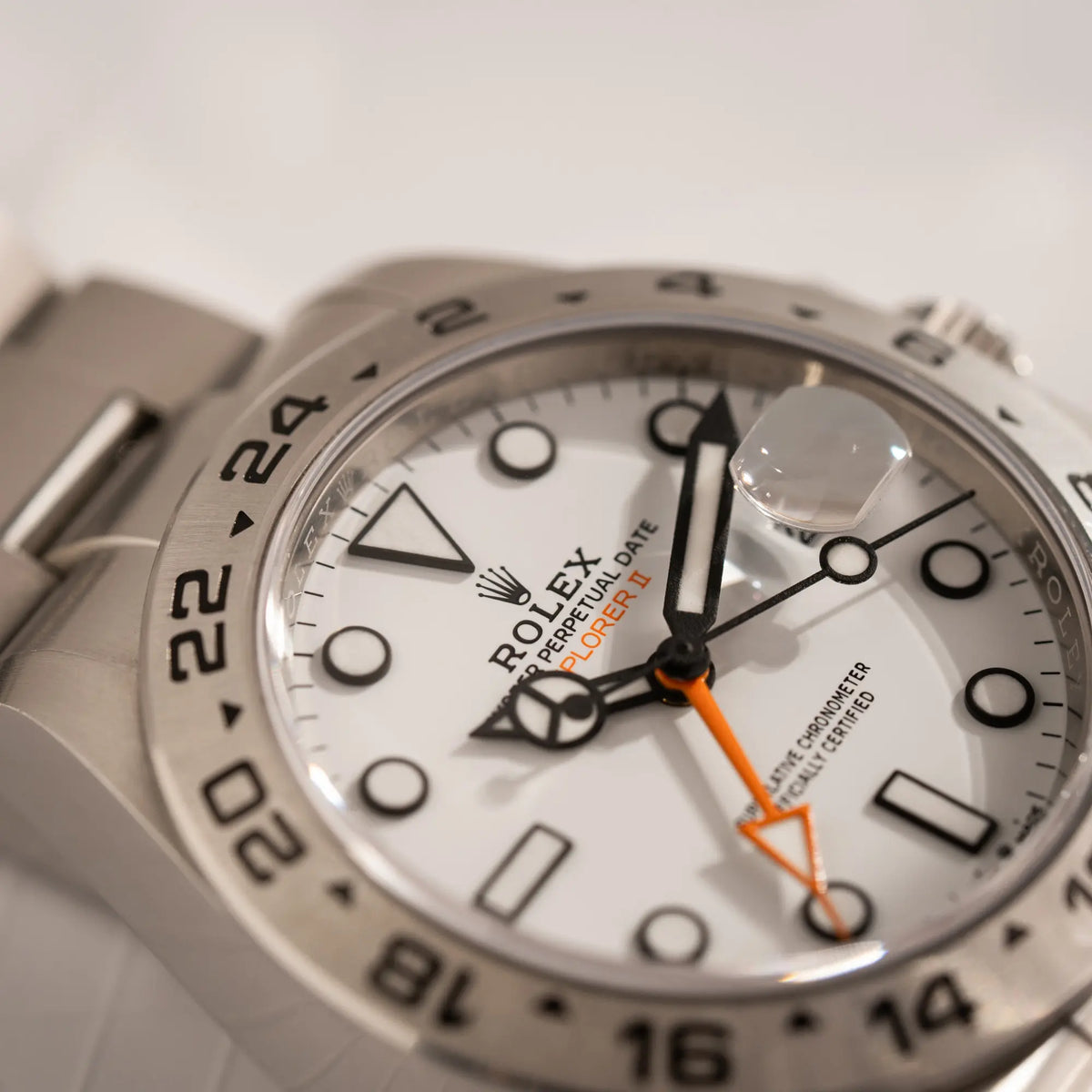 Detailaufnahme des Uhrenglases der Rolex Explorer II der Referenz 226570 am Oyster-Stahlband mit dem weißen Polar-Zifferblatt und dem typischen orangen 24-Stunden-Zeiger zeigt die Datumslupe