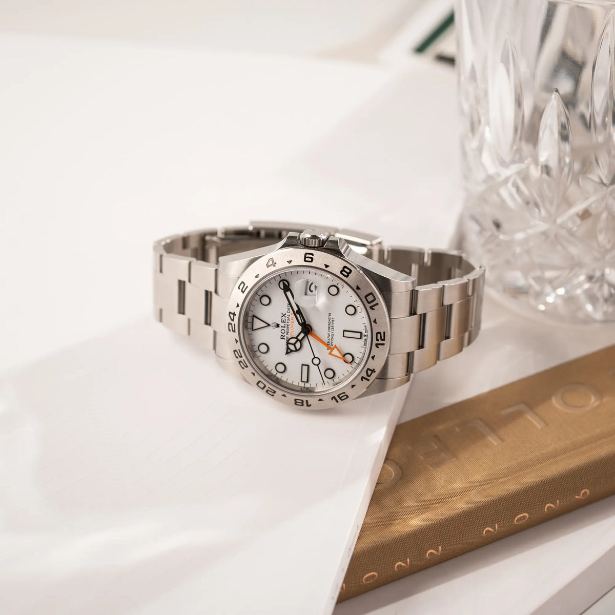 Produktfotografie der seitlich auf dem Uhrengehäuse liegenden Rolex Explorer II der Referenz 226570 am Oyster-Stahlband mit dem weißen Polar-Zifferblatt und dem typischen orangen 24-Stunden-Zeiger