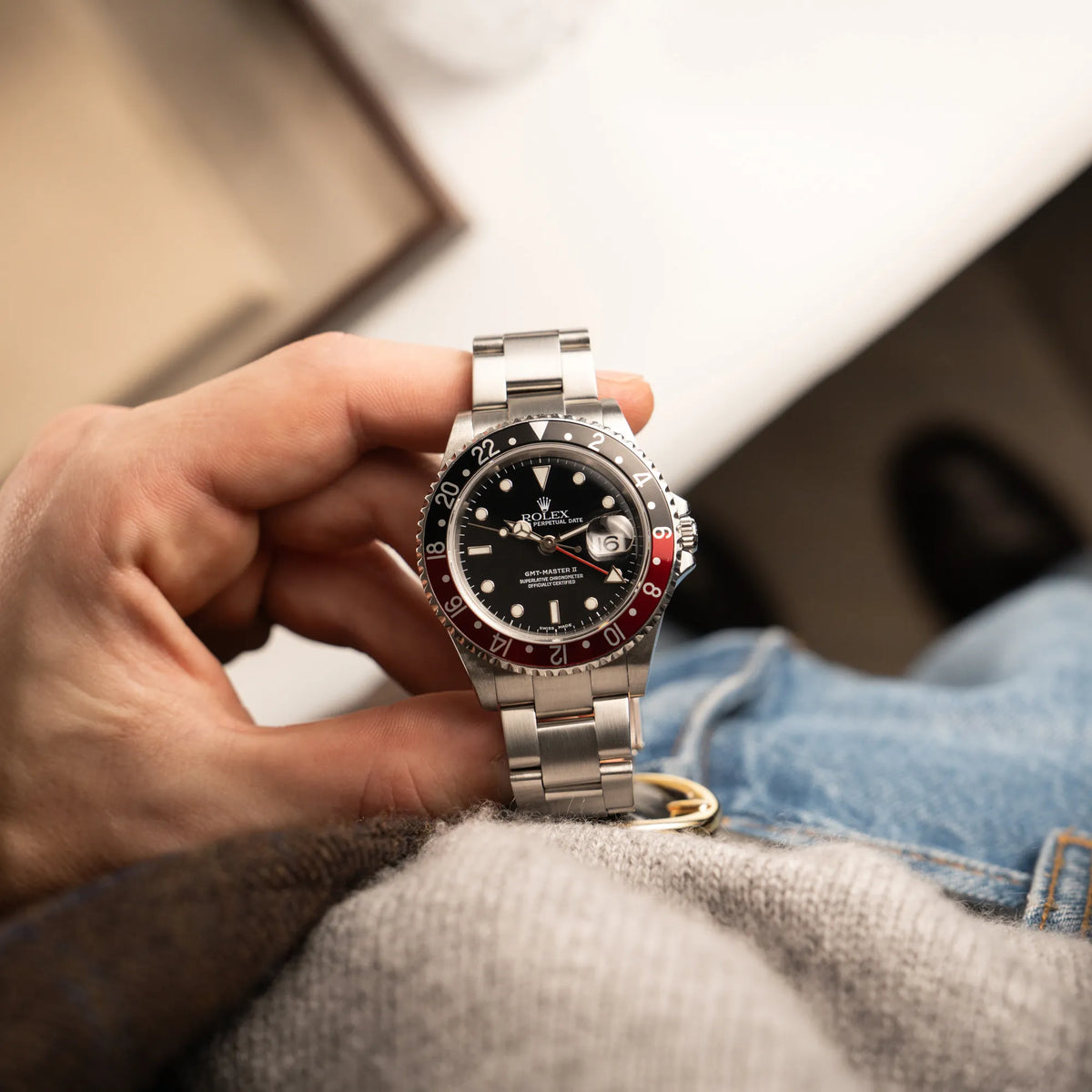 Mann hält die Rolex GMT-Master II 16710 mit der schwarz-roten "Coke" Aluminium-Lünetten-Einlage aus 2003 am Oyster Stahlband in seiner Hand und präsentiert die Uhr in die Kamera