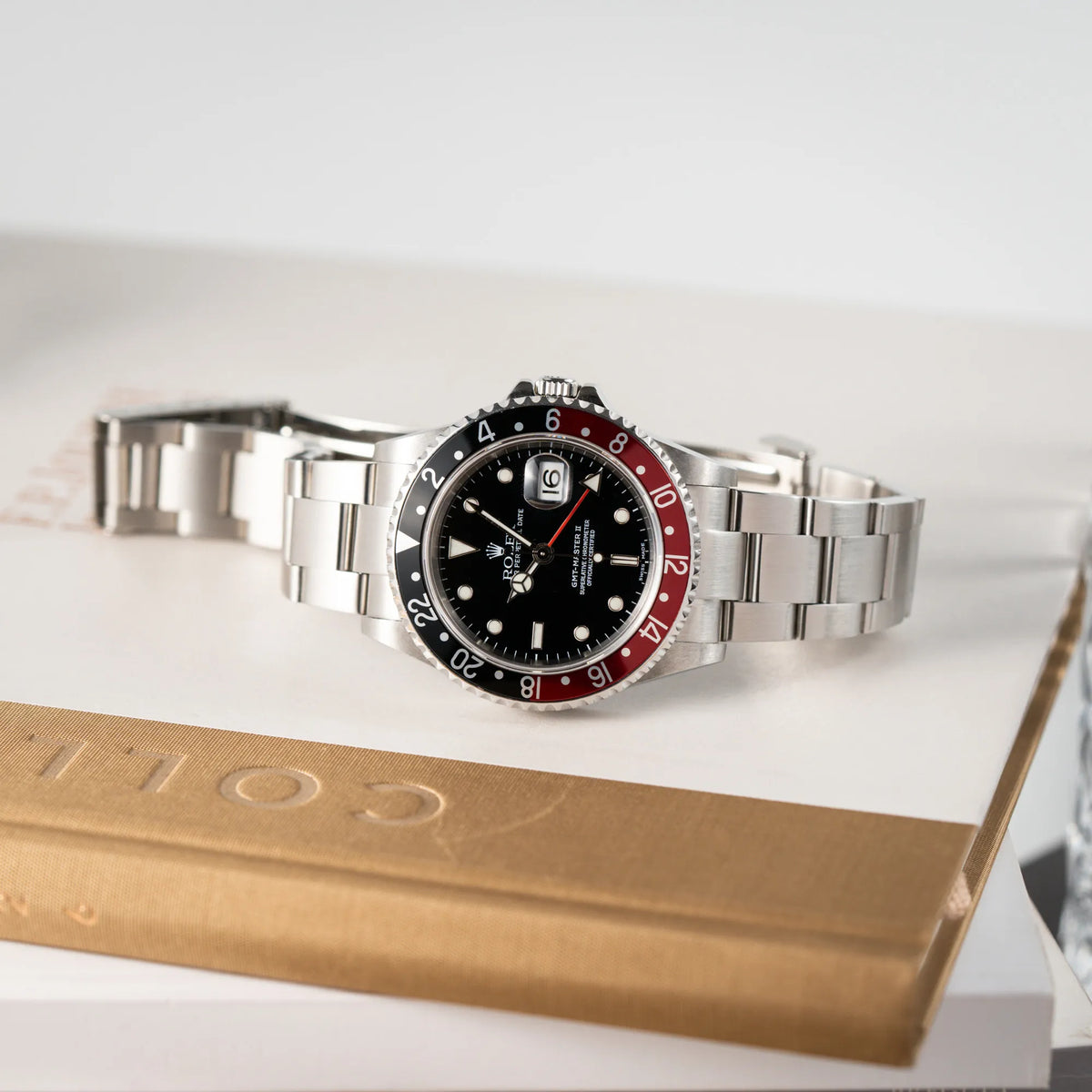 Produktfotografie der seitlich auf dem Gehäuse liegenden Rolex GMT-Master II 16710 mit der schwarz-roten "Coke" Aluminium-Lünetten-Einlage aus 2003 am Oyster Stahlband