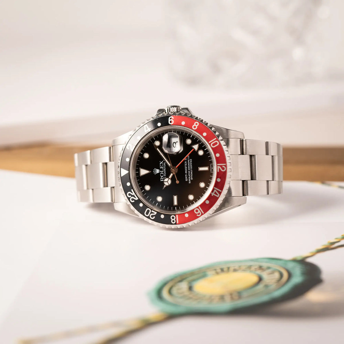 Produktfotografie der seitlich auf dem Uhrengehäuse liegenden Rolex GMT-Master II der Referenz 16710 2000 mit schwarz-roter Coke-Lünette und dem für das Jahr 2000 typische "Swiss Only" - Zifferblatt