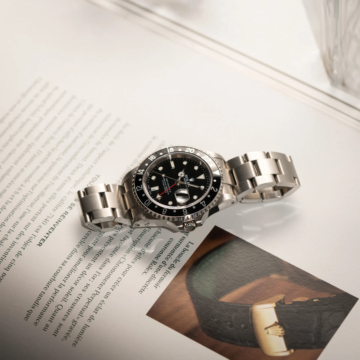 Produktfotografie der Rolex GMT-Master II 16710 aus 2001 mit schwarzem Aluminium-Lünetten-Inlay in einem neuwertigen Zustand während die Uhr auf einem Uhrenbuch über Rolex liegt