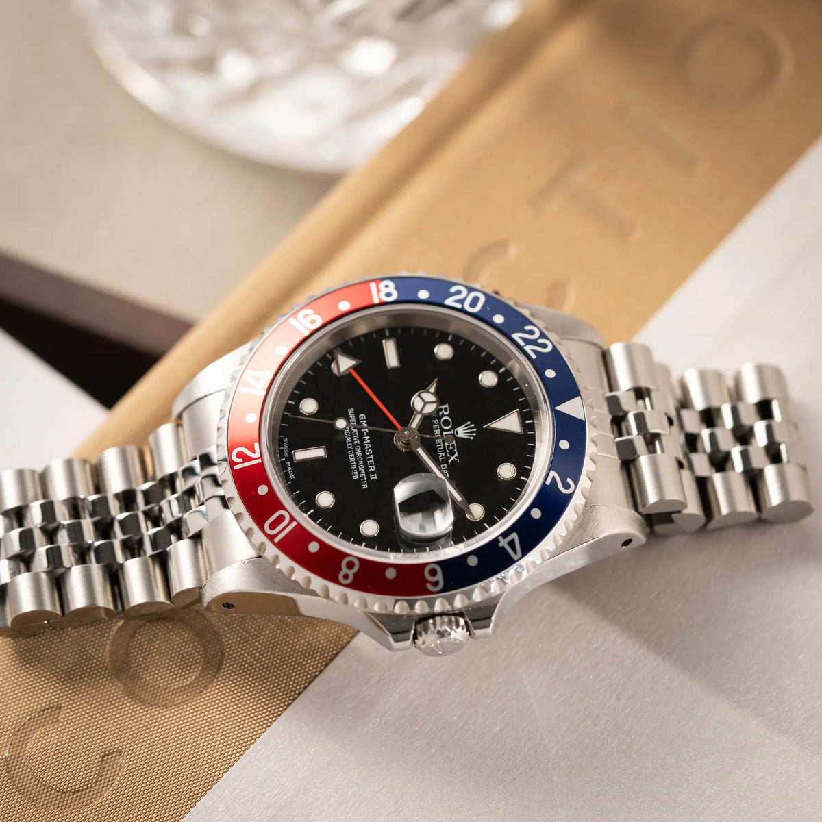 Produktfotografie der flach auf einem Buch liegenden Rolex GMT-Master II 16710 mit der blau-roten Pepsi-Lünette am Jubilee-Armband