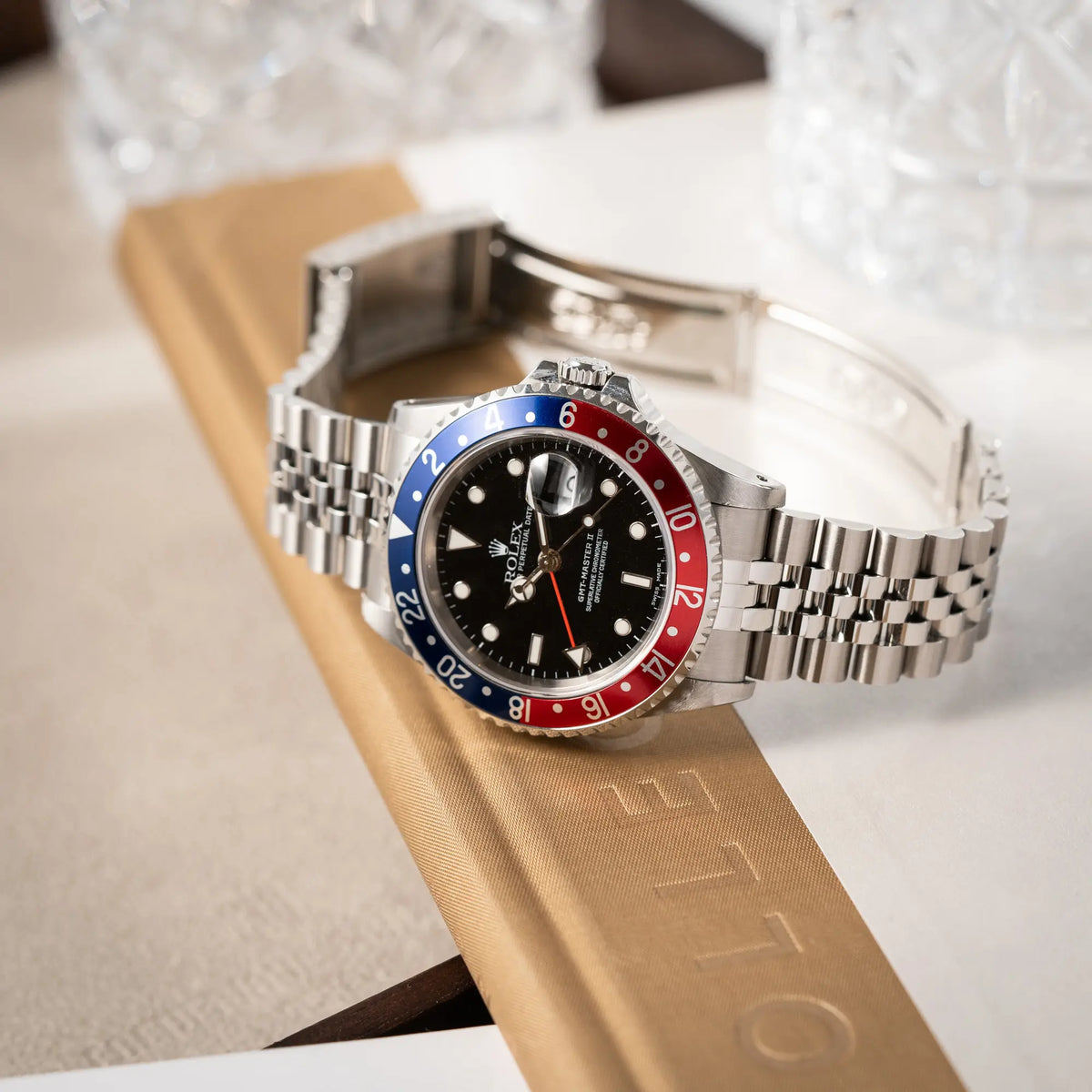 Produktfoto der Rolex GMT-Master II 16710 mit der blau-roten Pepsi-Lünette am Jubilee-Armband während die Uhr mit geöffneter Schliesse auf einem Buch liegt