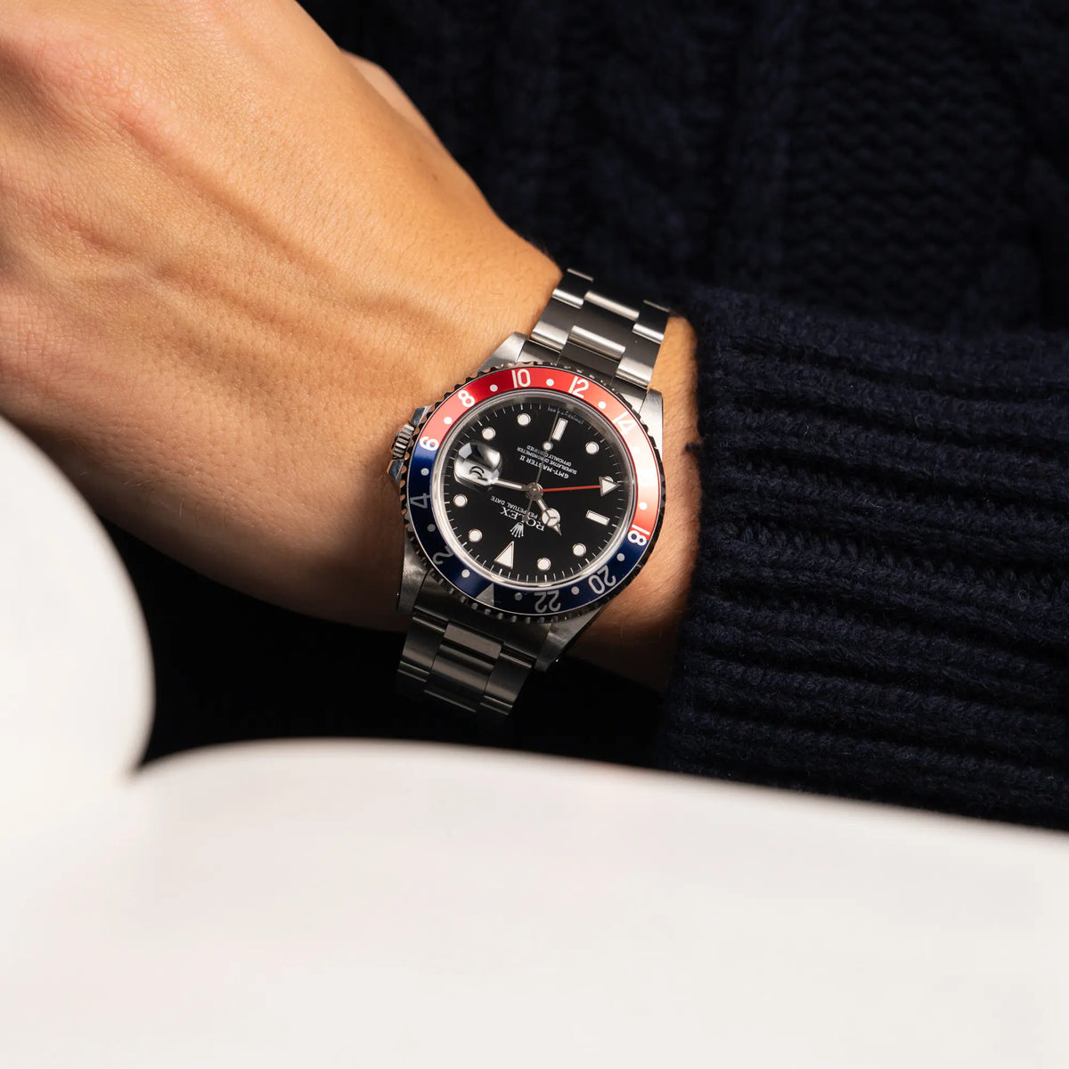Mann in blauem Stickpullover trägt die Rolex GMT Master 2 der Referenz 16710 aus der T-Serie mit blau-roter Pepsi-Lünette an seinem Handgelenk