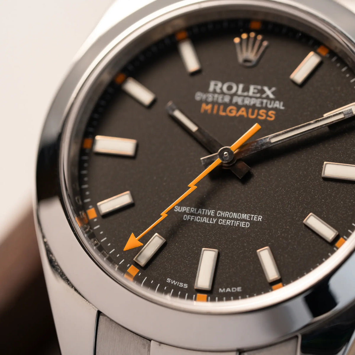 Detailaufnahme der Rolex Milgauss der Referenz 116400 mit schwarzem Zifferblatt und orangen Akzenten mit Fokus auf dem orangen, blitzförmigen Sekundenzeiger
