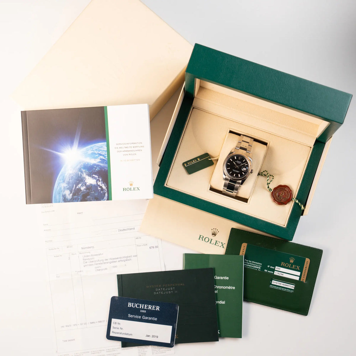 Rolex Oyster Perpetual Date 34 der Referenz 115234 mit schwarzem Zifferblatt und der geriffelten Weißgold-Lünette zusammen mit dem Lieferumfang, bestehend aus Box, Umkarton, Booklets, Garantiekarte, Service-Beleg und Hangatag