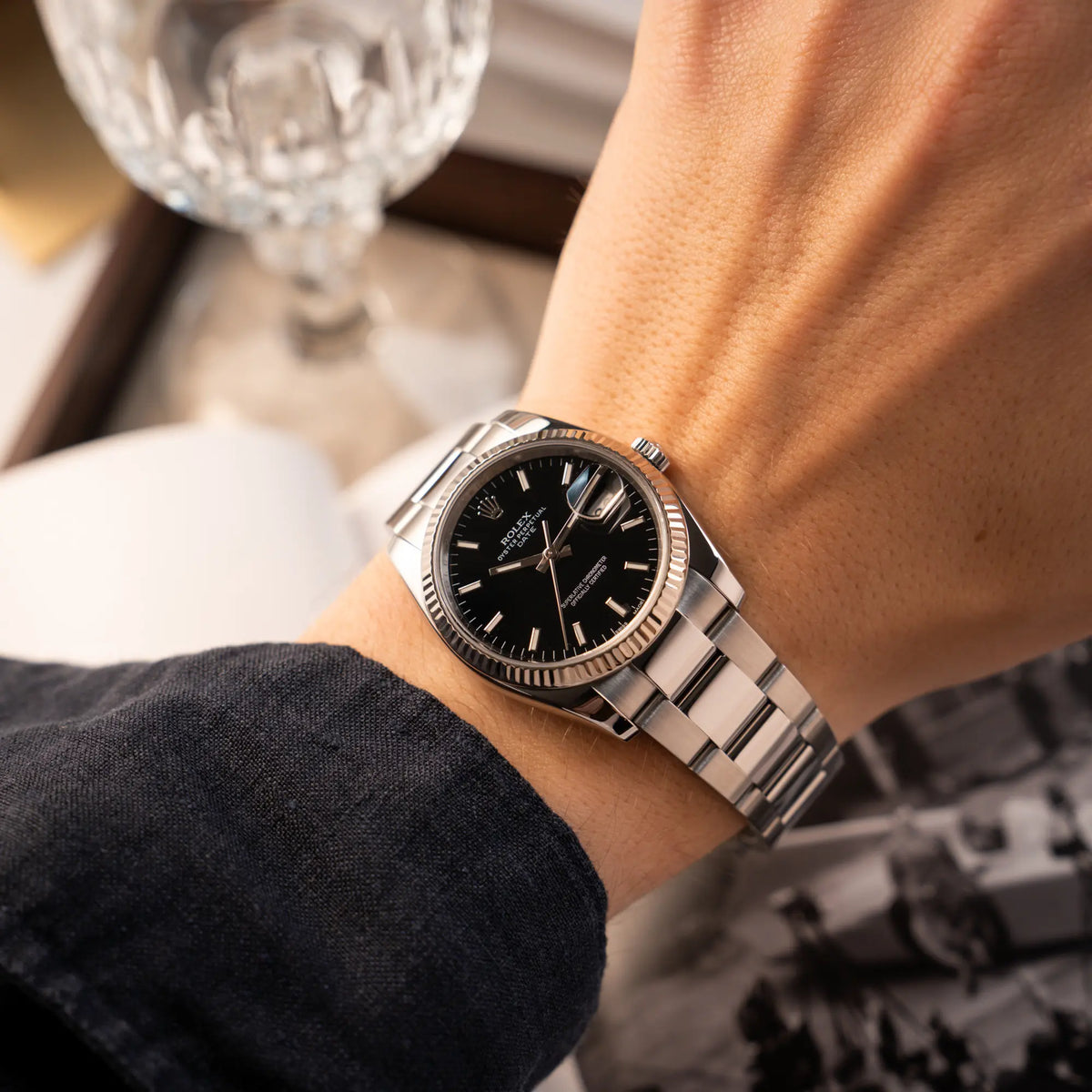 Mann trägt die Rolex Oyster Perpetual Date 34 der Referenz 115234 mit schwarzem Zifferblatt und der geriffelten Weißgold-Lünette für einen Wristshot am Handgelenk