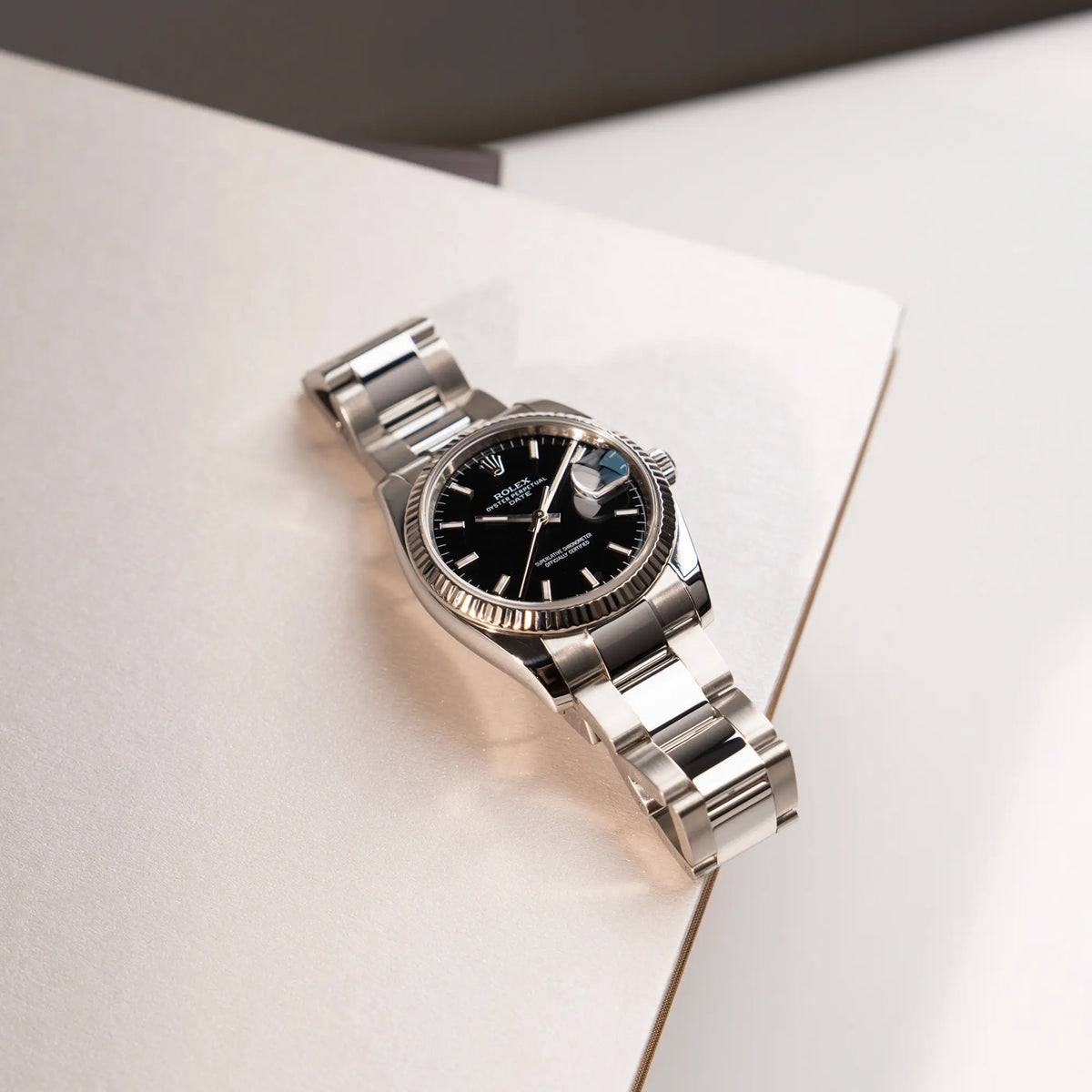 Produktfotografie der Rolex Oyster Perpetual Date 34 der Referenz 115234 mit schwarzem Zifferblatt und der geriffelten Weißgold-Lünette