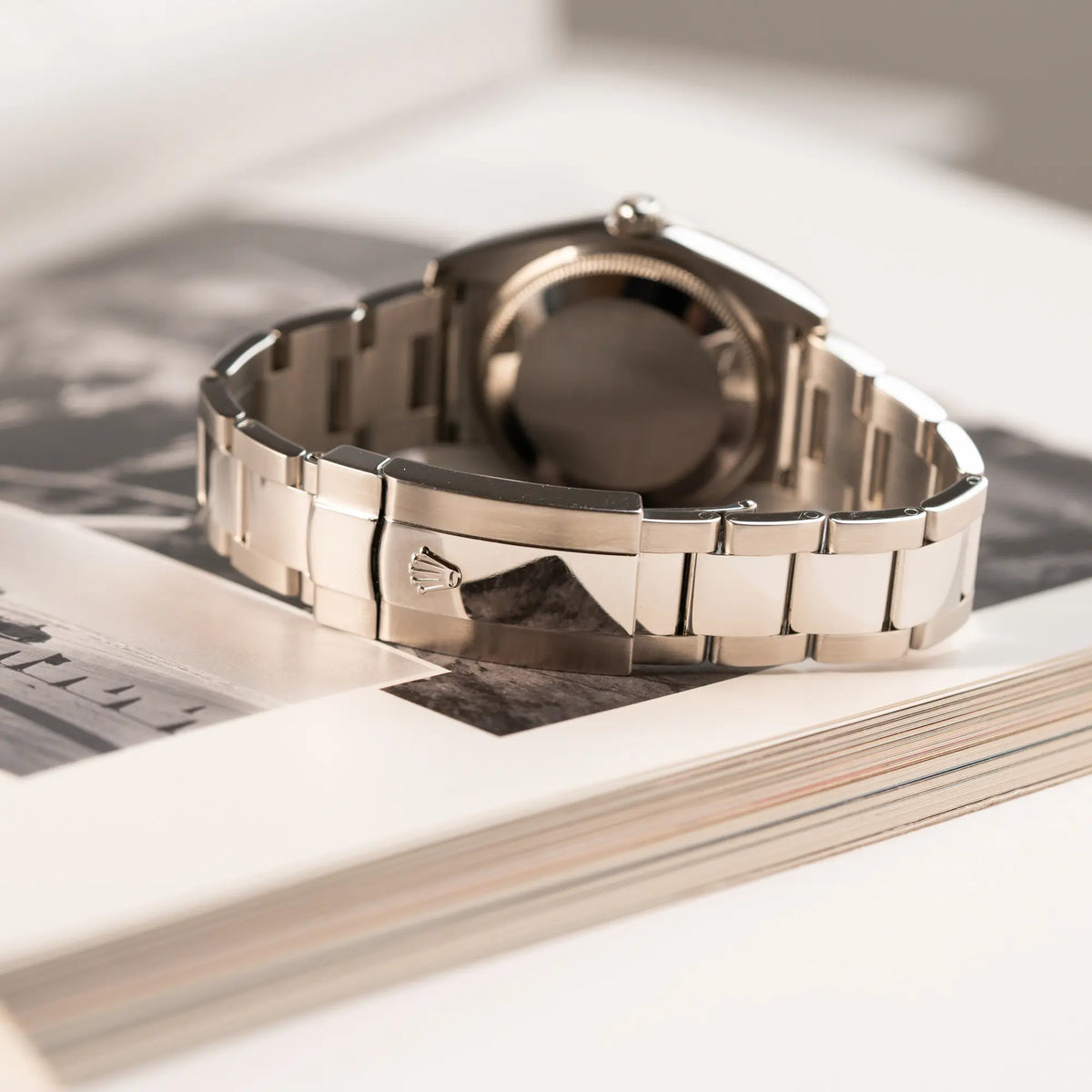 Produktfotografie der Rolex Oyster Perpetual Date 34 der Referenz 115234 mit schwarzem Zifferblatt und der geriffelten Weißgold-Lünette zeigt die Oyster-Faltschliesse
