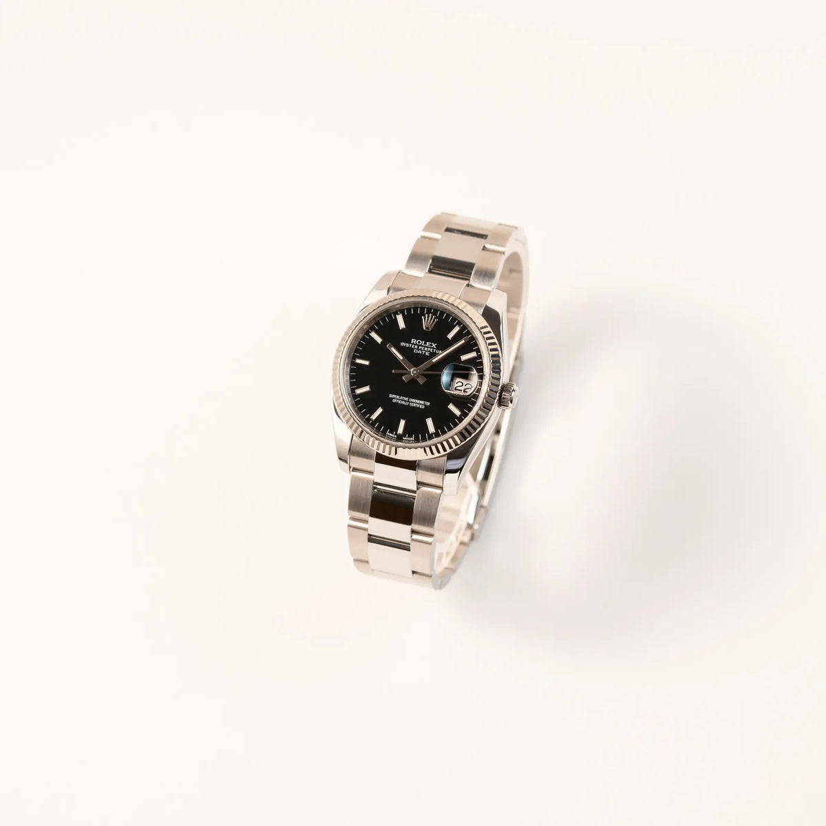 Leicht schräge Ansicht der Rolex Oyster Perpetual Date 34 der Referenz 115234 mit schwarzem Zifferblatt und der geriffelten Weißgold-Lünette