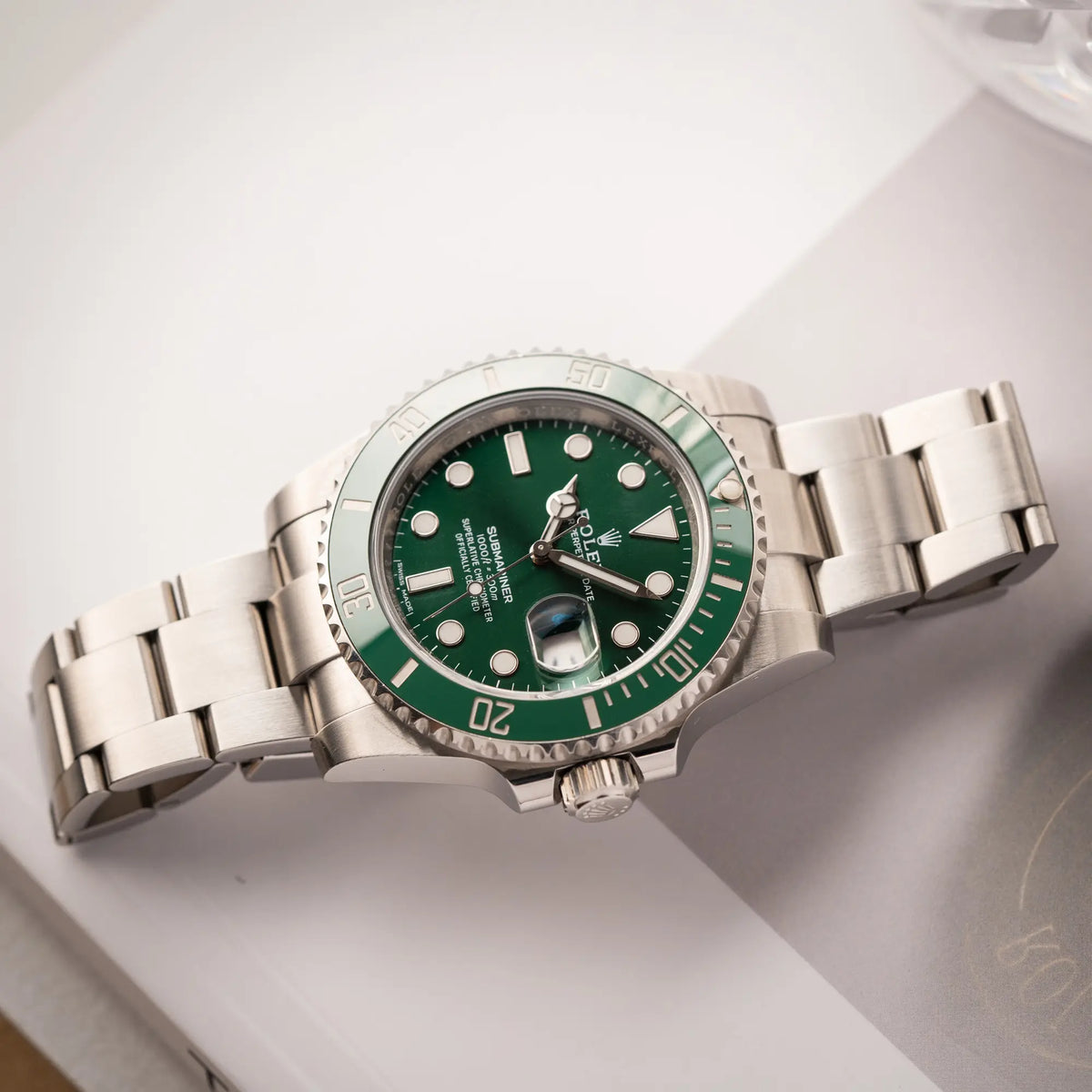 Produktfotografie zeigt die flach liegende Rolex Submariner Date 116610LV, Nickname "HULK", mit dem grünen Zifferblatt und der grünen Keramik-Lünette, an dem klassischen Oyster-Stahl-Armband