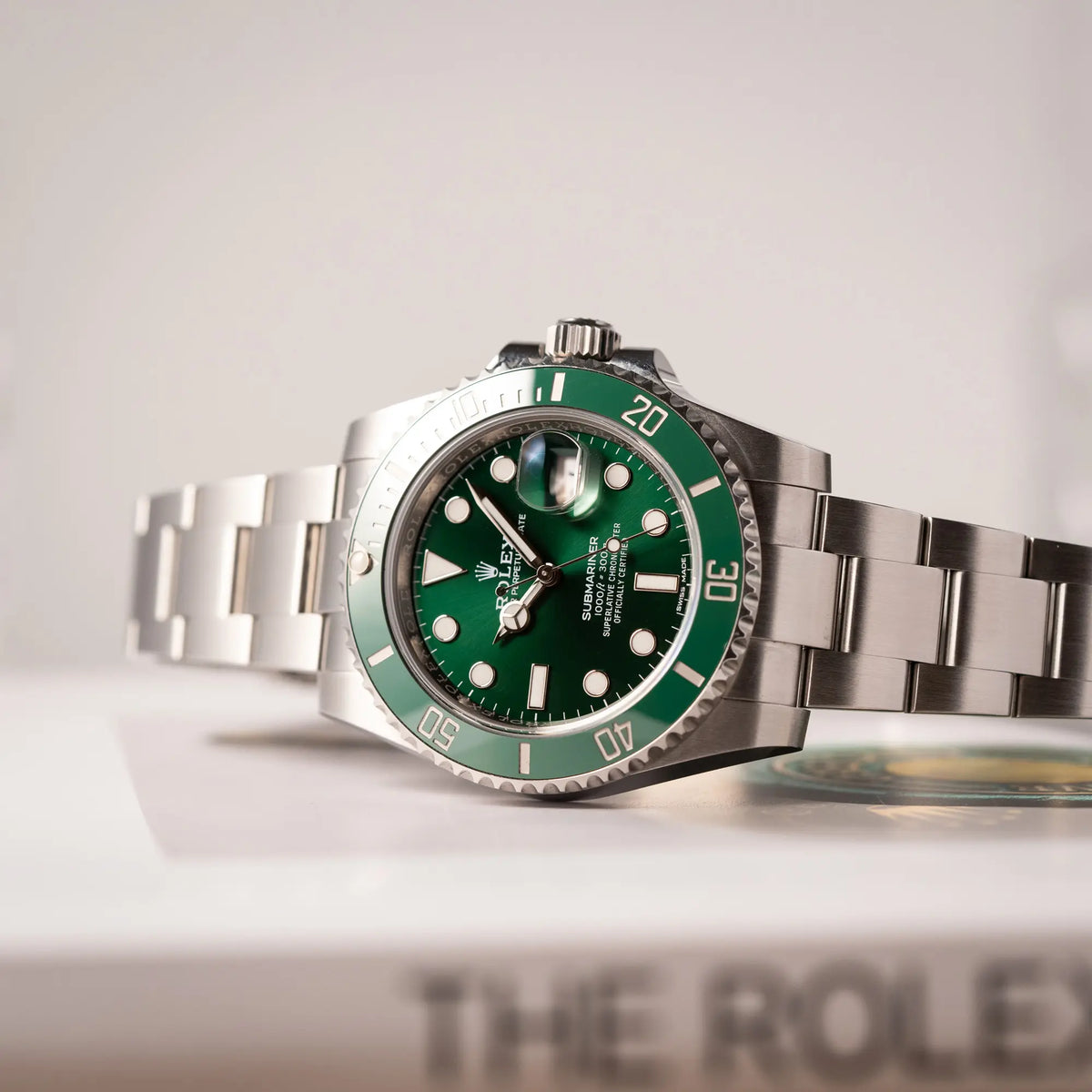 Produktfotografie zeigt die seitlich auf dem Uhrengehäuse liegende Rolex Submariner Date 116610LV, Nickname "HULK", mit dem grünen Zifferblatt und der grünen Keramik-Lünette, an dem klassischen Oyster-Stahl-Armband